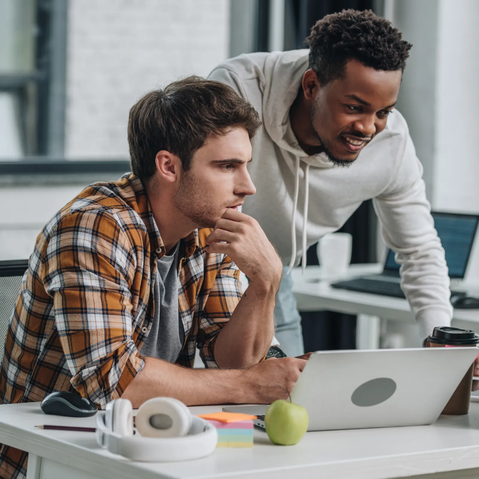Two young men collaborating on a laptop and desktop computer in a modern office setting