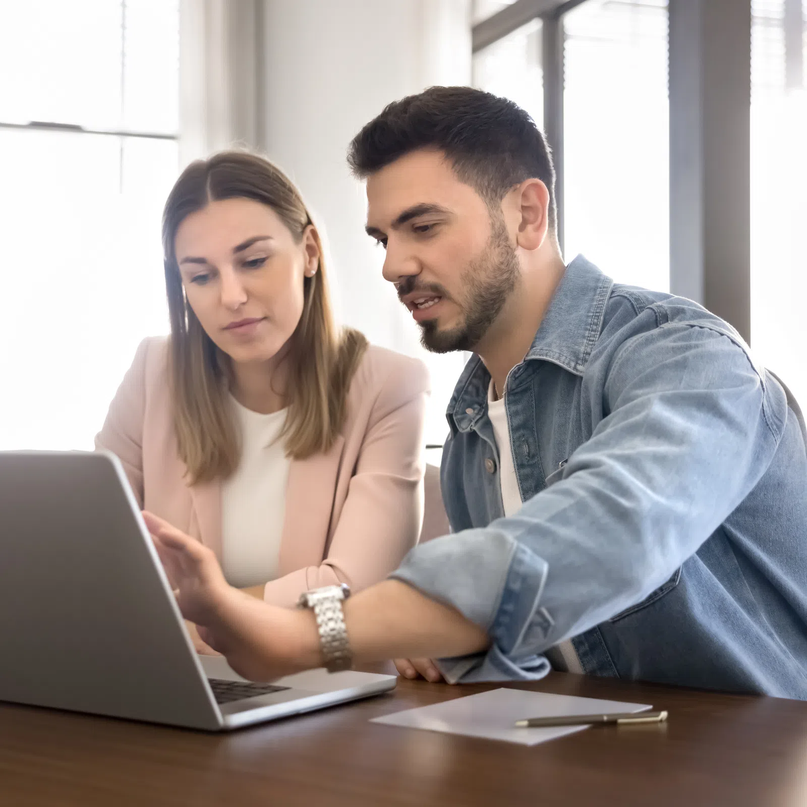 Man and woman discussing work on laptop in bright office setting