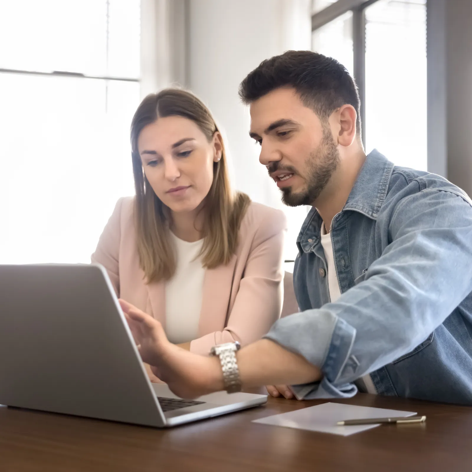 Three coworkers focused and collaborating while looking at a desktop monitor in a modern office setting.
