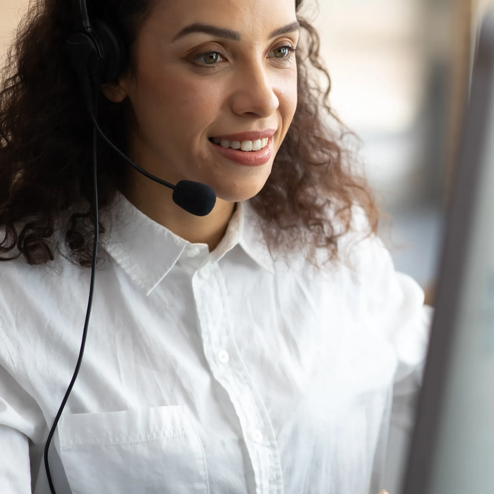 Smiling woman wearing a headset working on a computer in a bright office setting