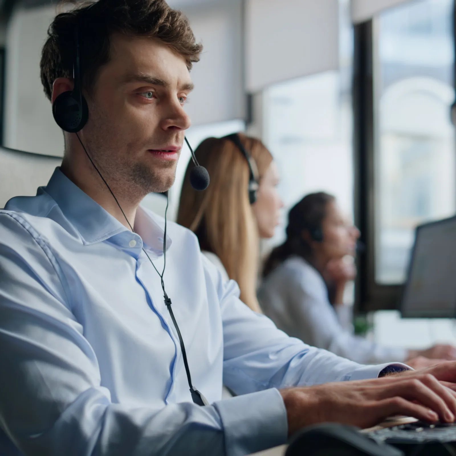 Customer service representatives wearing headsets working on computers in a modern office environment.