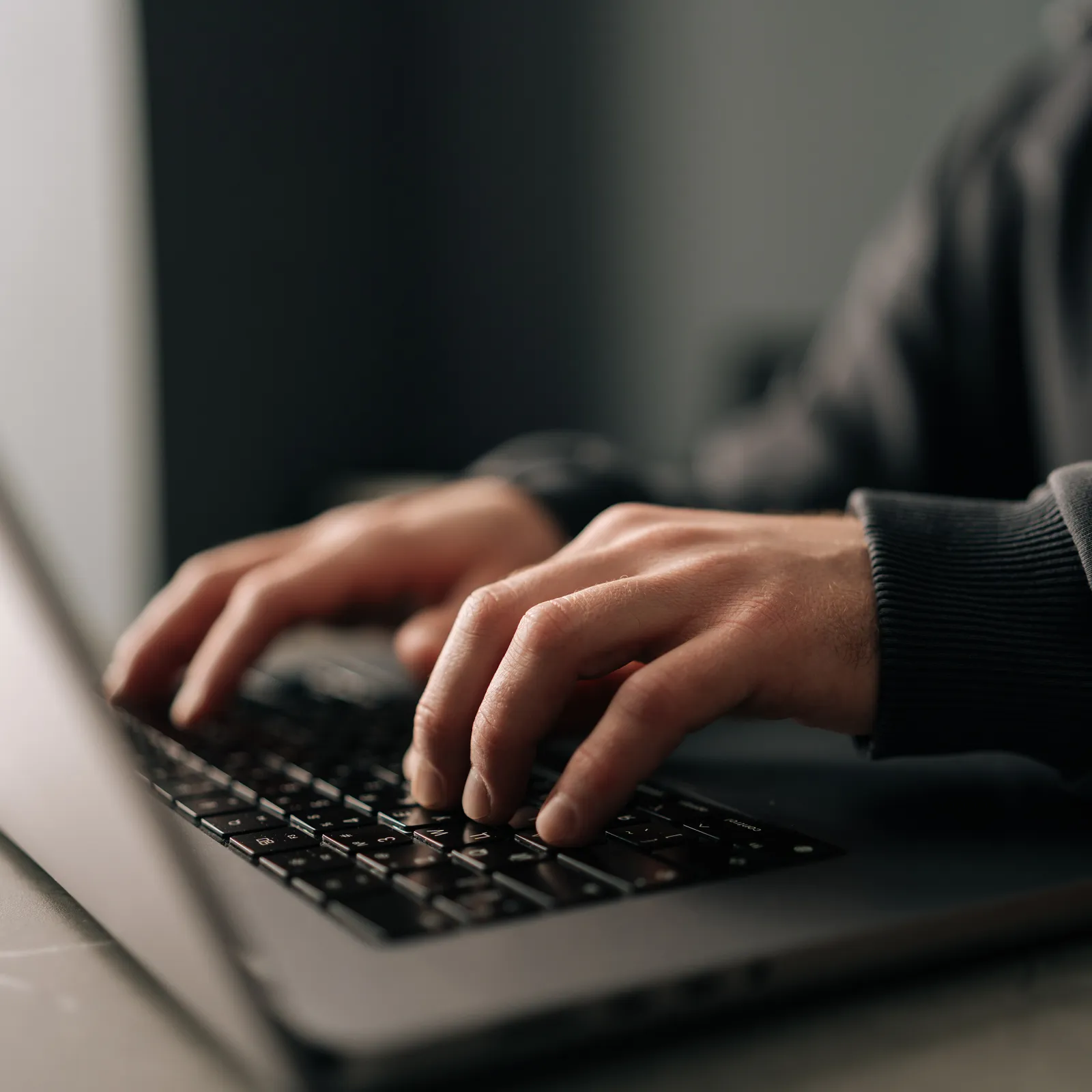 Close-up of hands typing on a laptop keyboard with soft natural lighting on a gray surface.