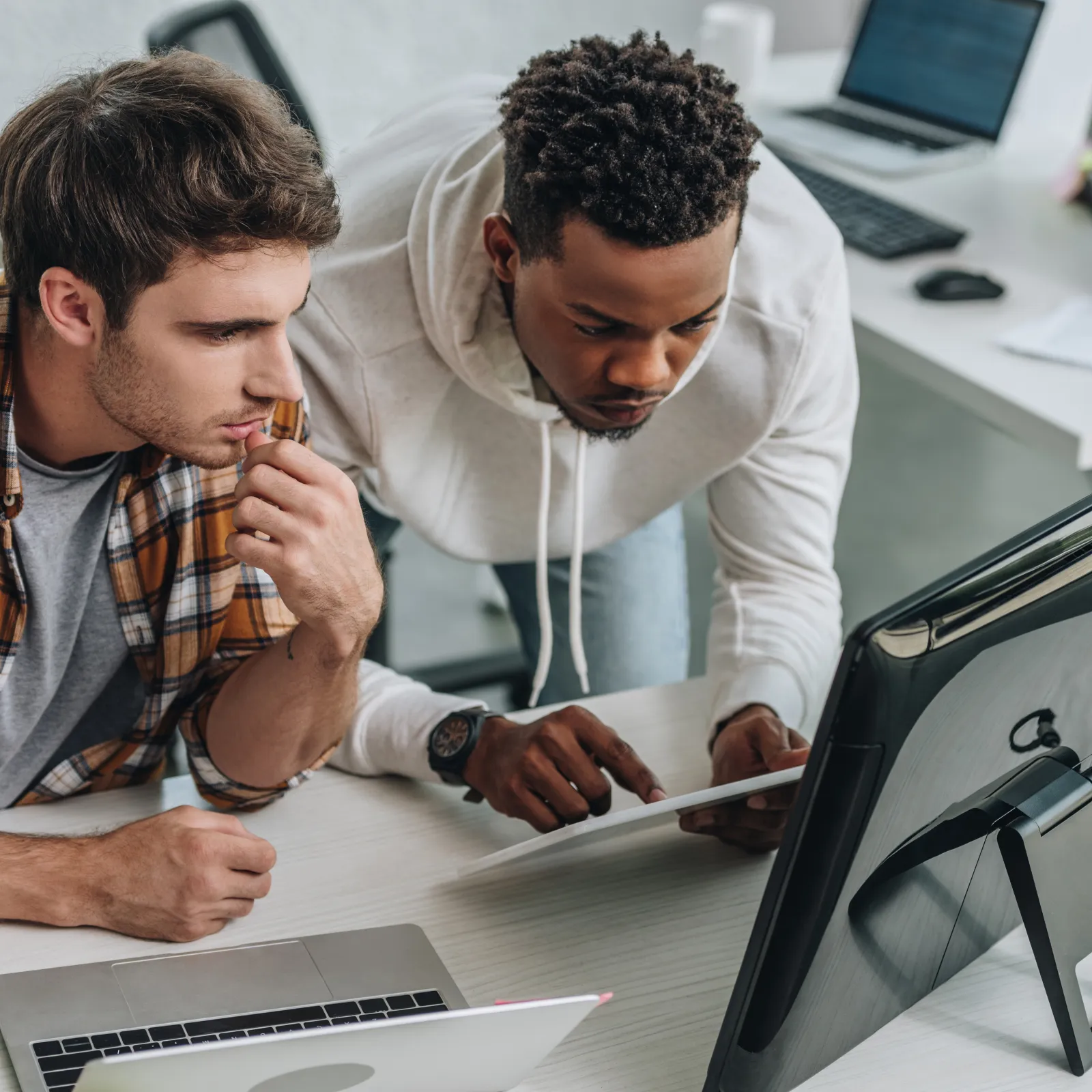 Three coworkers focused and collaborating while looking at a desktop monitor in a modern office setting.