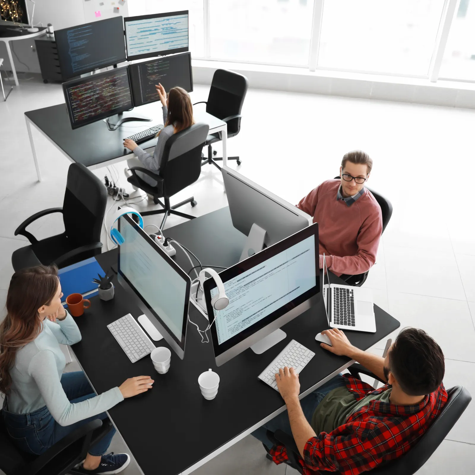 Team of software developers collaborating and coding at a modern office workspace with multiple monitors and laptops.