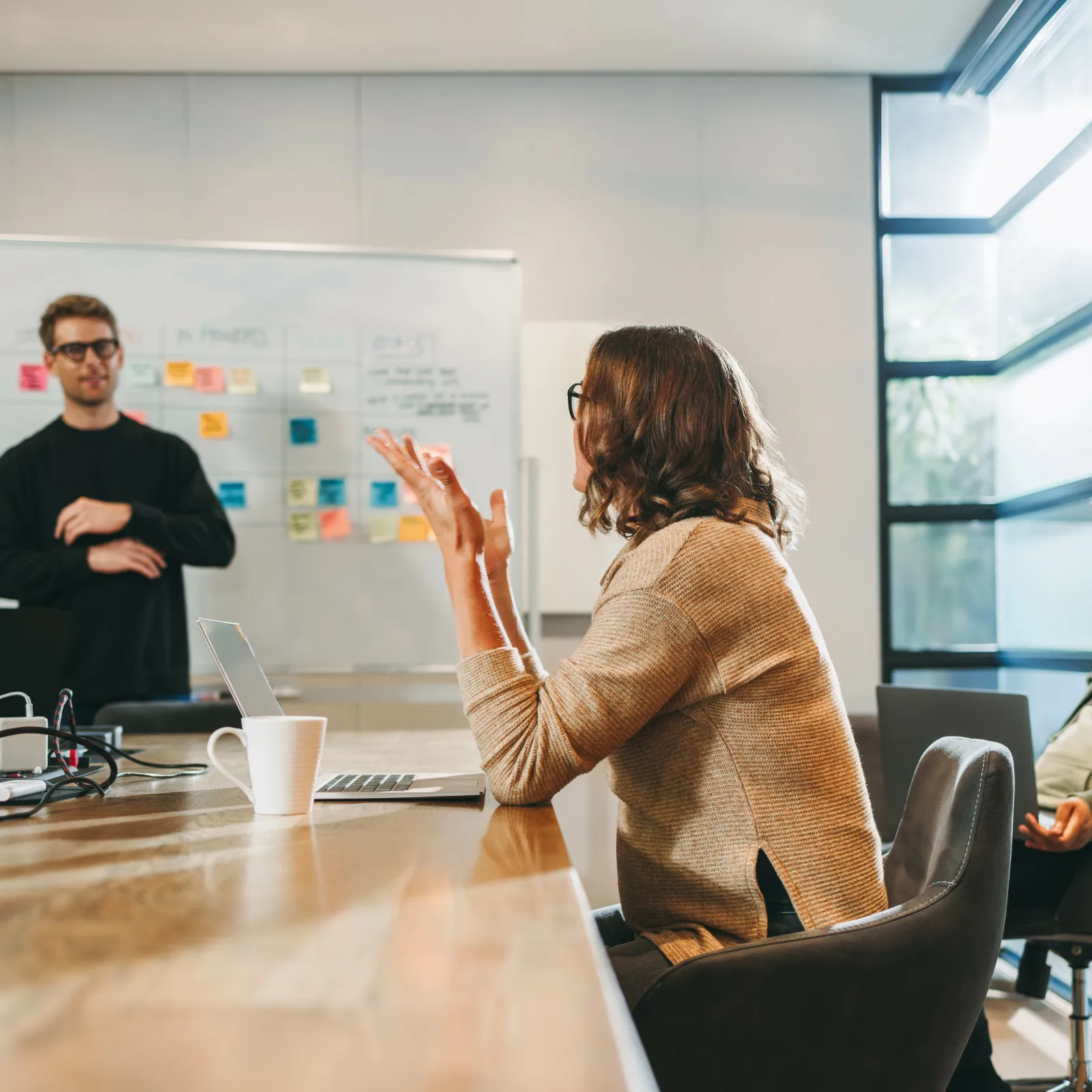 Business team discussing ideas around a table in a modern office with a whiteboard and laptops