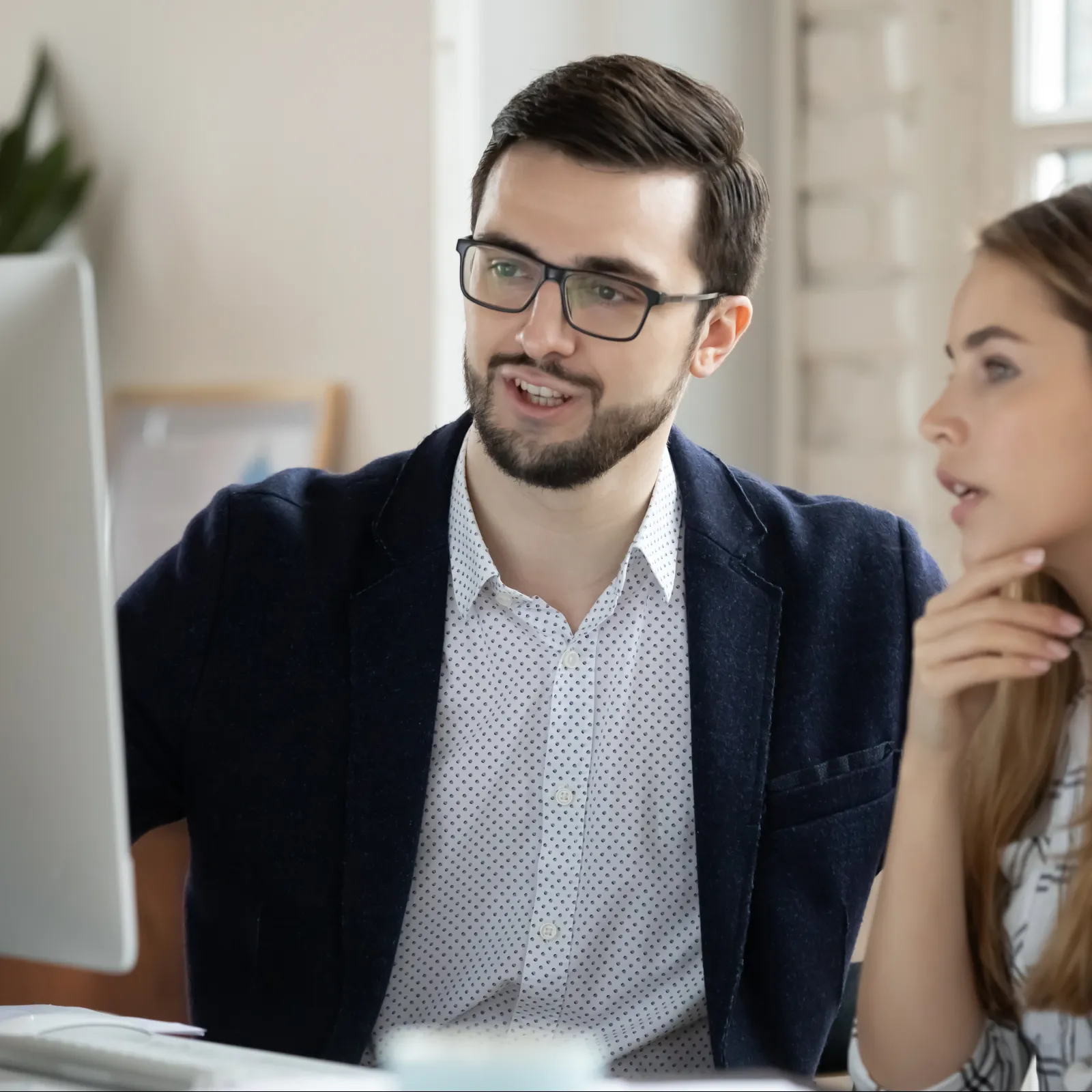 Man and woman collaborating and discussing work while looking at a computer screen in a bright office.