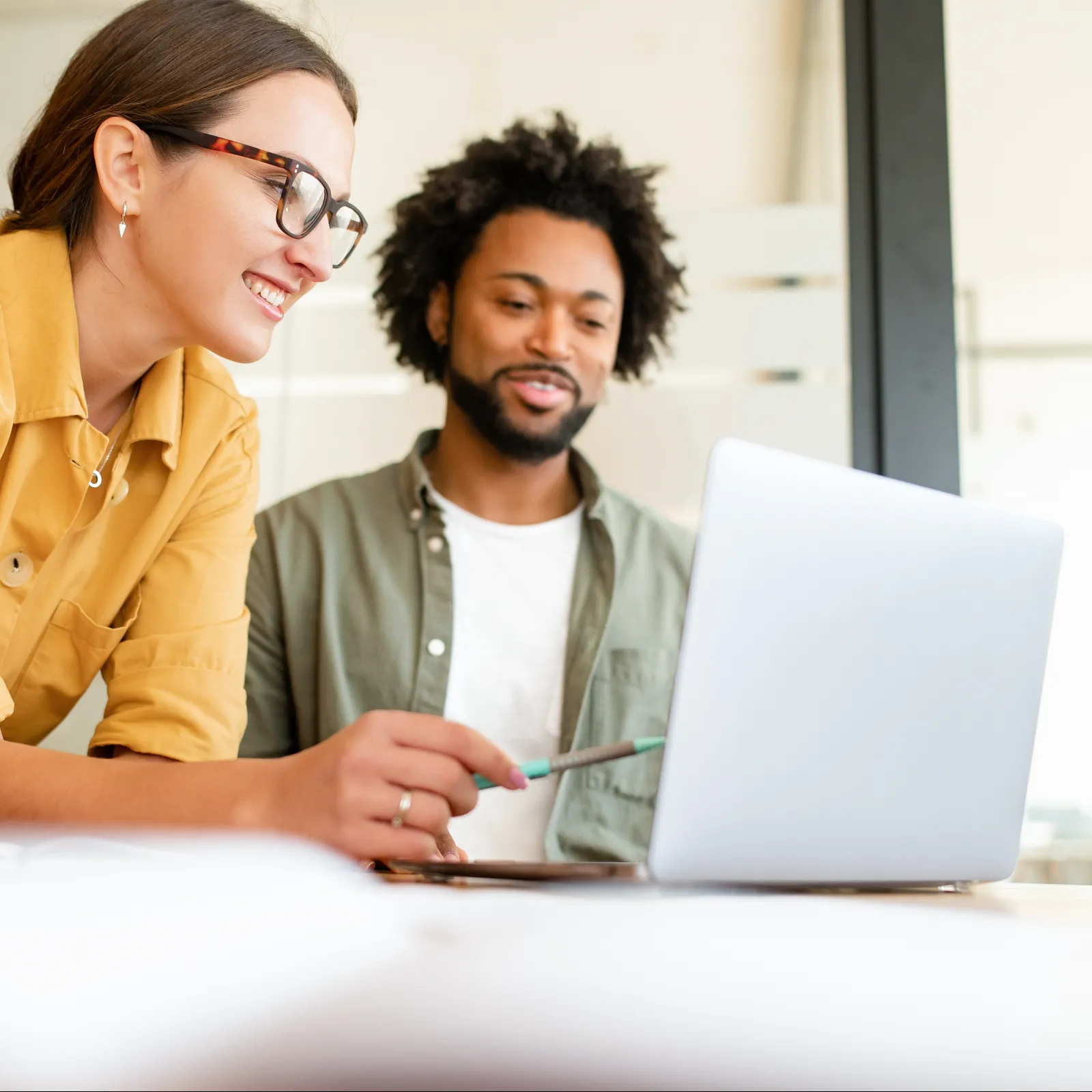 Two colleagues discussing work while looking at a laptop in a bright office setting