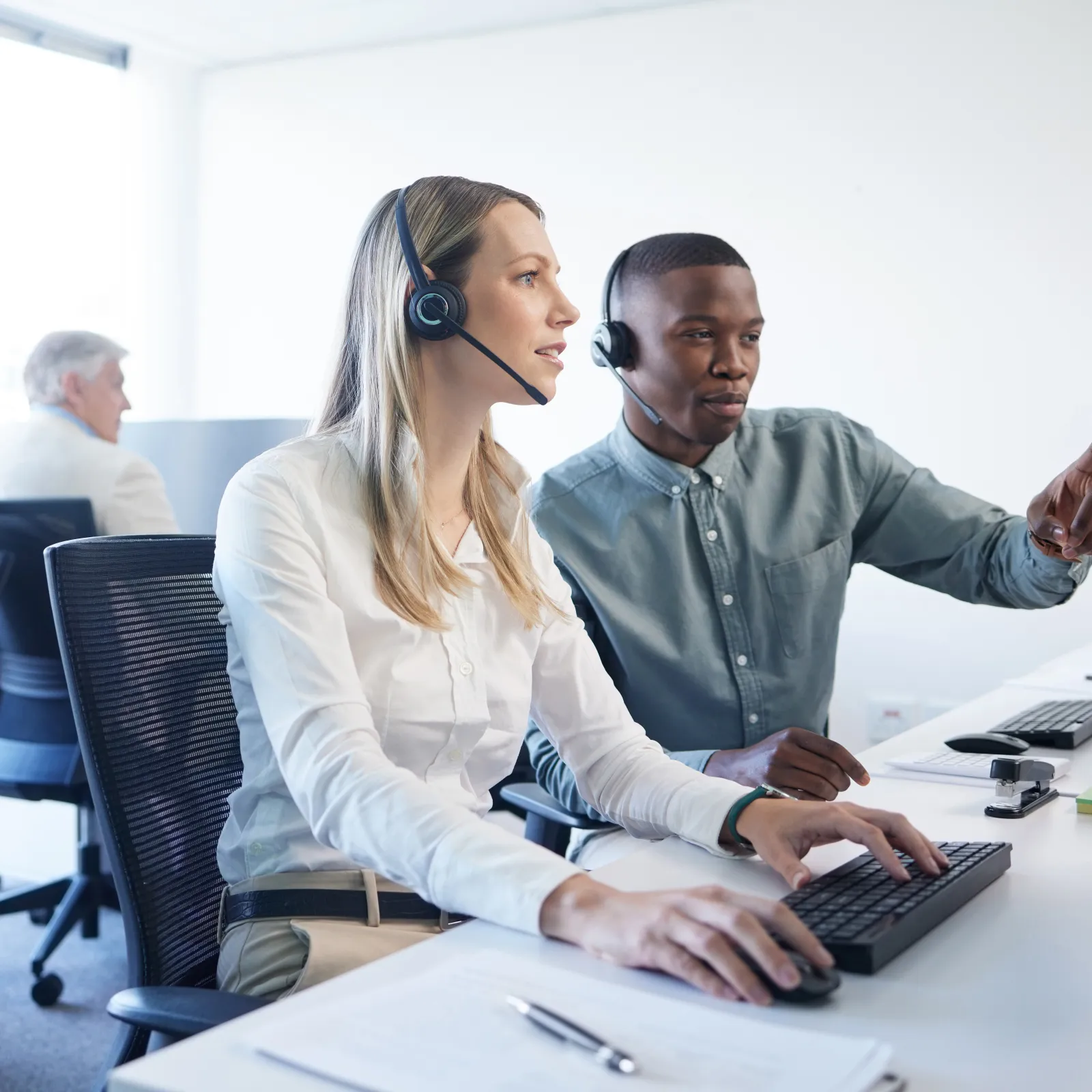 Customer support team wearing headsets working together at computers in a bright modern office environment