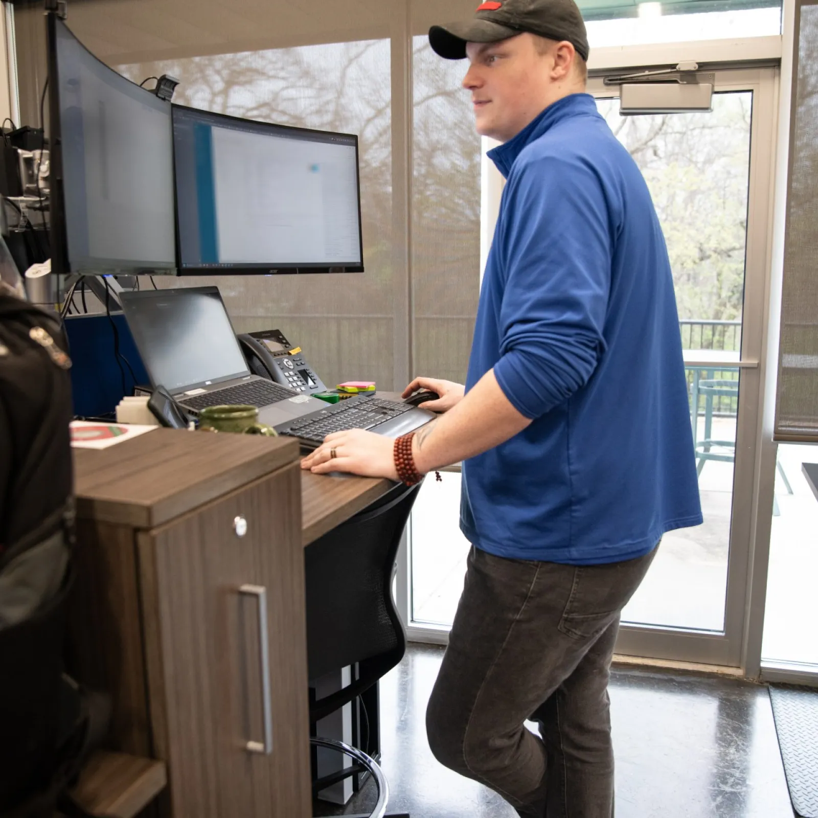 Person working at a standing desk with dual monitors in a modern office environment.