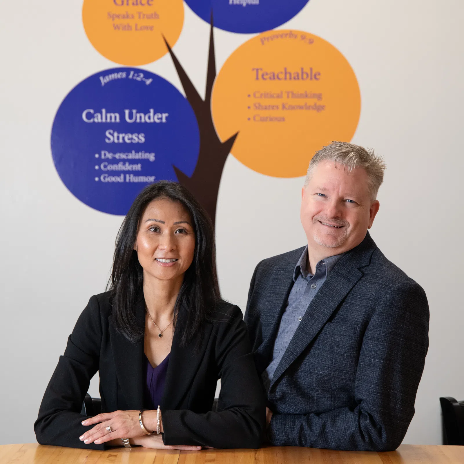 Professional couple posing in front of a tree-style wall mural with values and principles.
