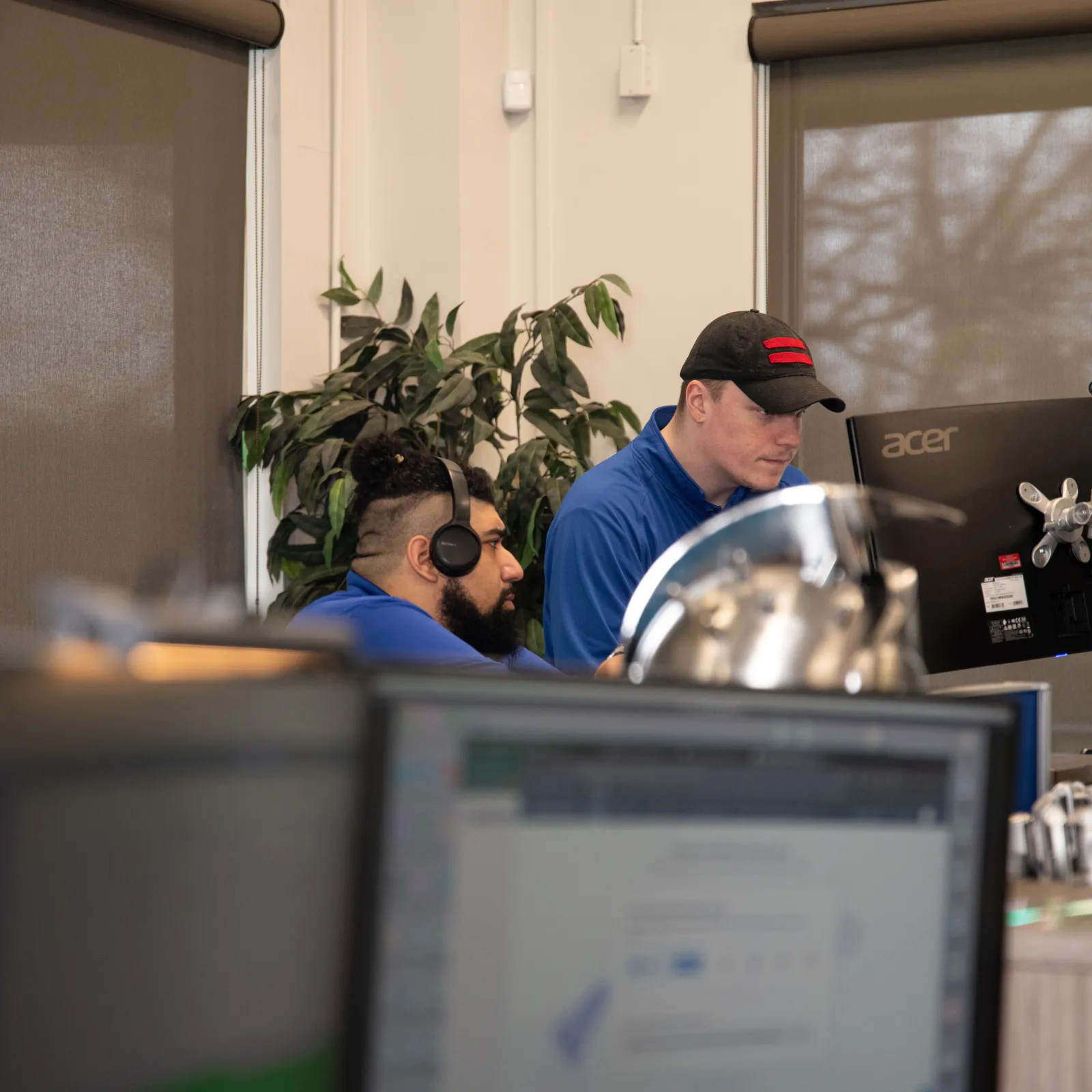 Two professionals working at computers in a modern office environment, wearing headsets and focused on tasks.