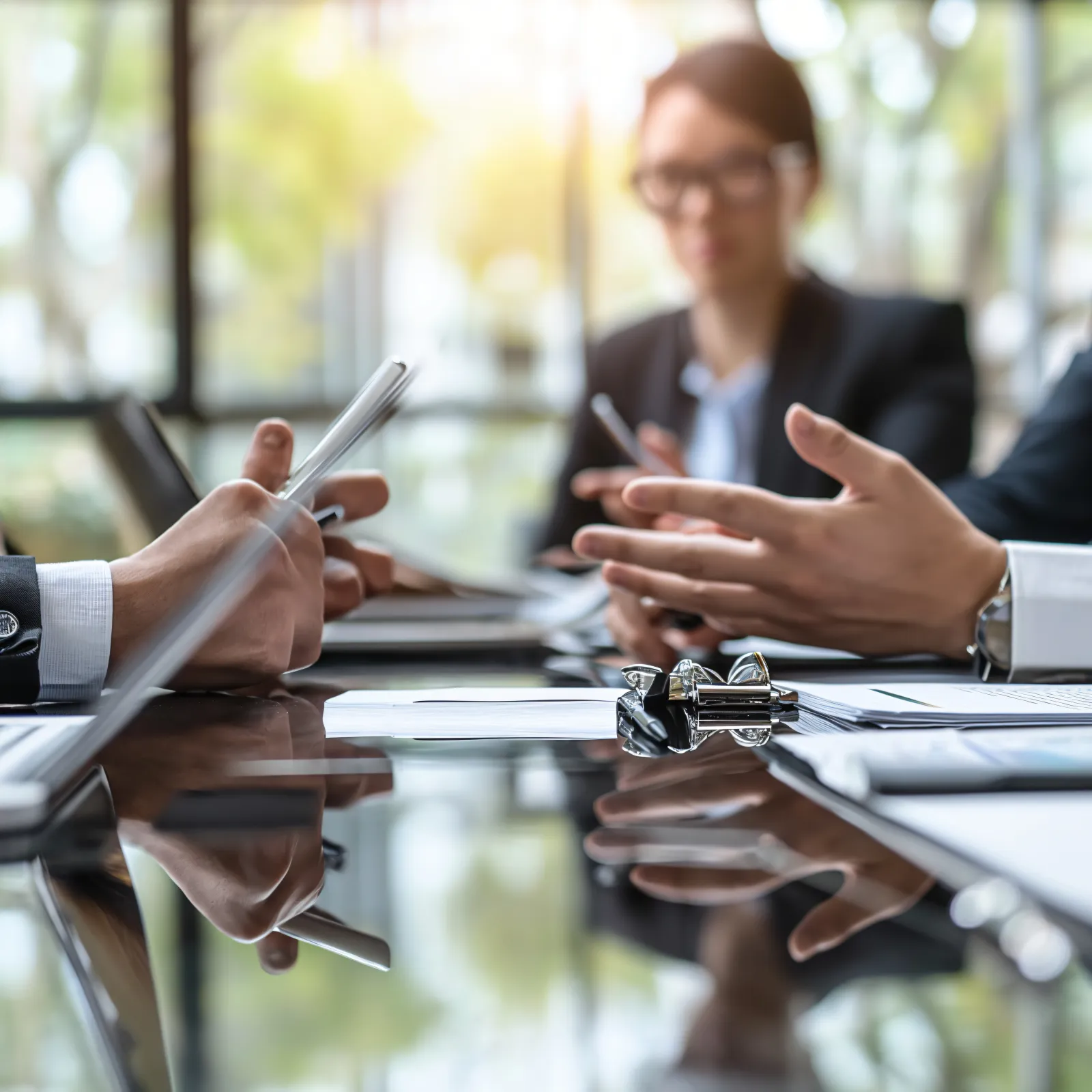 Business professionals in suits engaged in a meeting around a glossy conference table with documents and laptops.