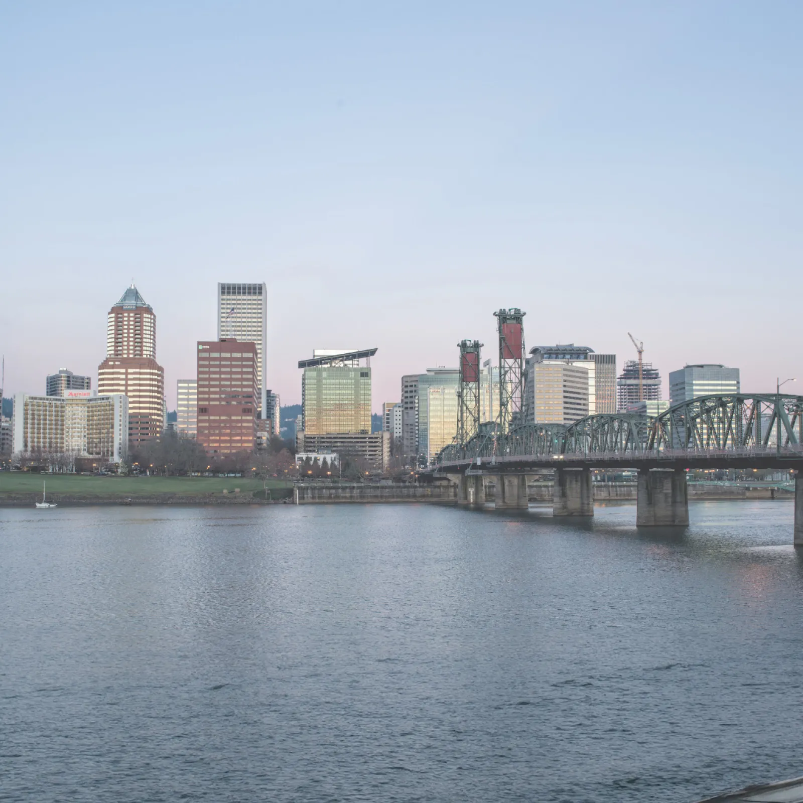 Portland city skyline with waterfront and Steel Bridge at dusk under clear blue sky