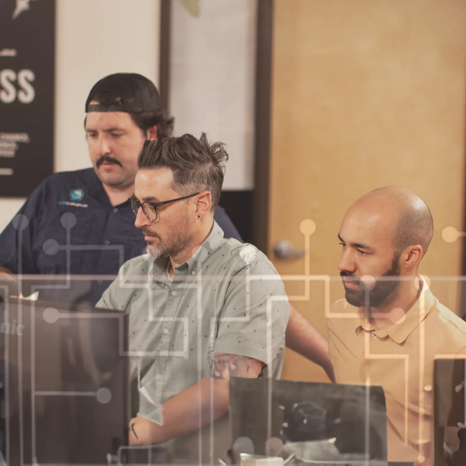 Three men collaborating and working together in an office setting on desktop computers
