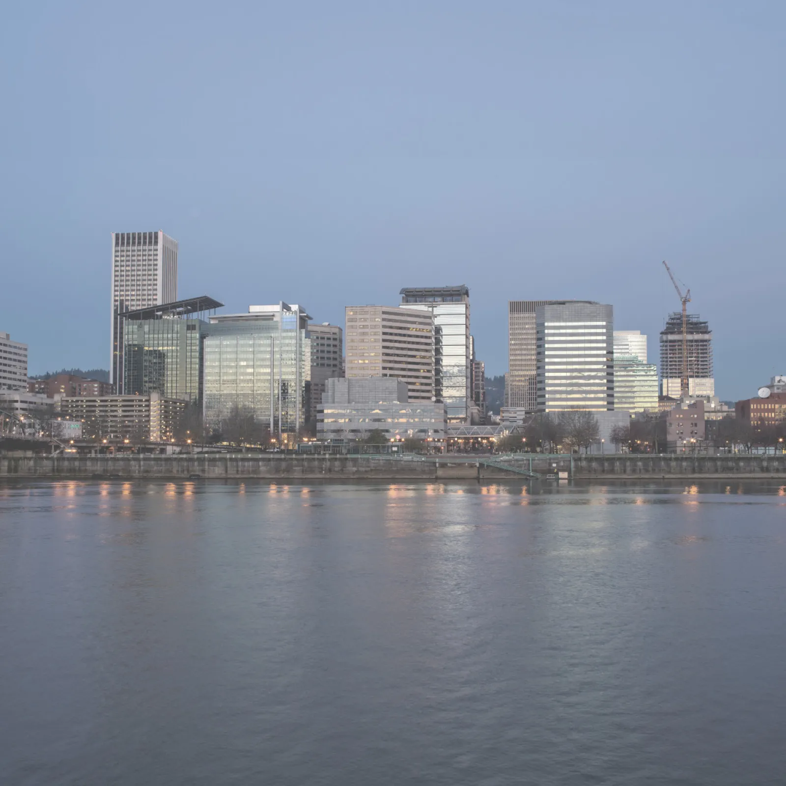 City skyline with modern skyscrapers reflected in a calm river at dusk under a clear sky