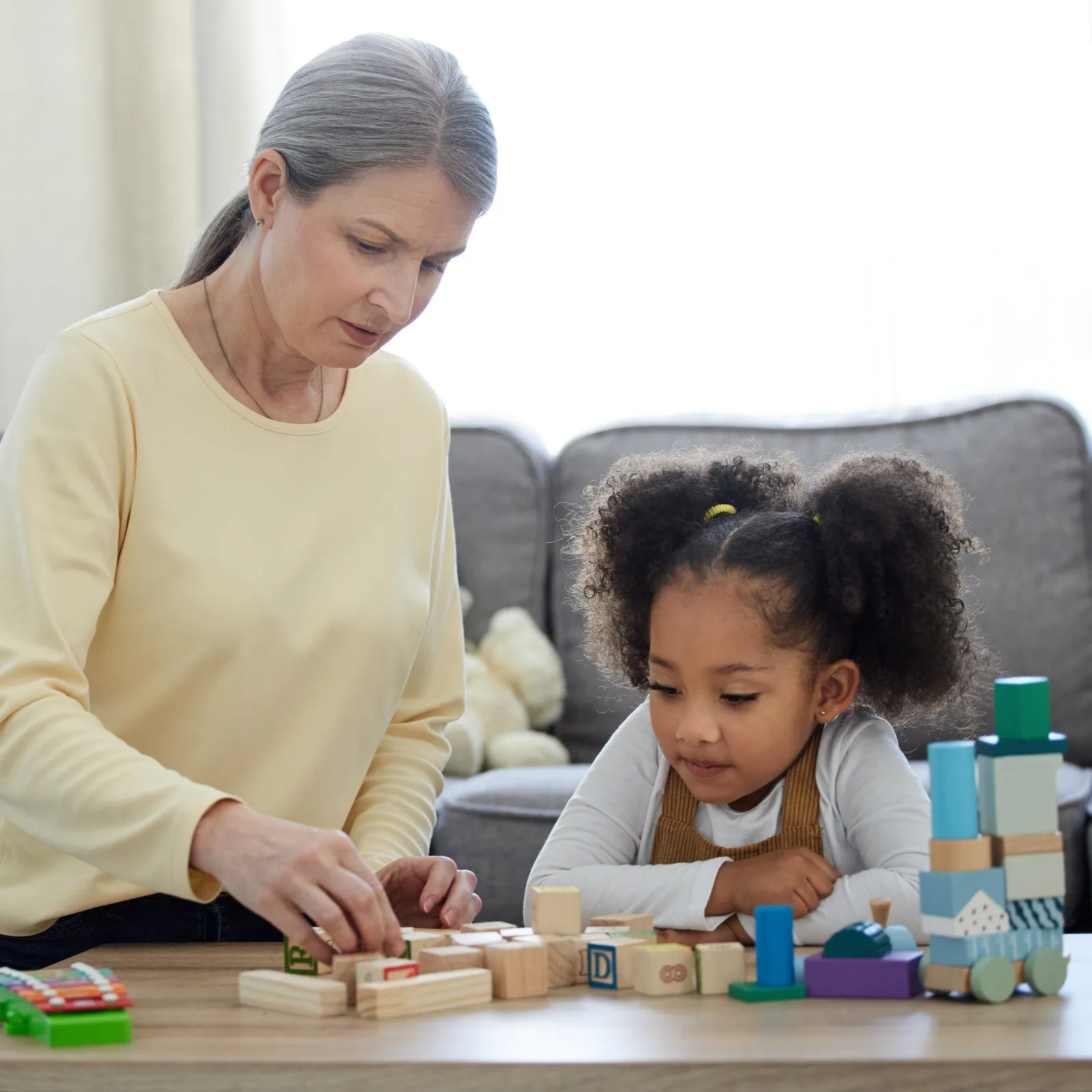 Older woman and young girl playing with wooden blocks together on a table in a living room.