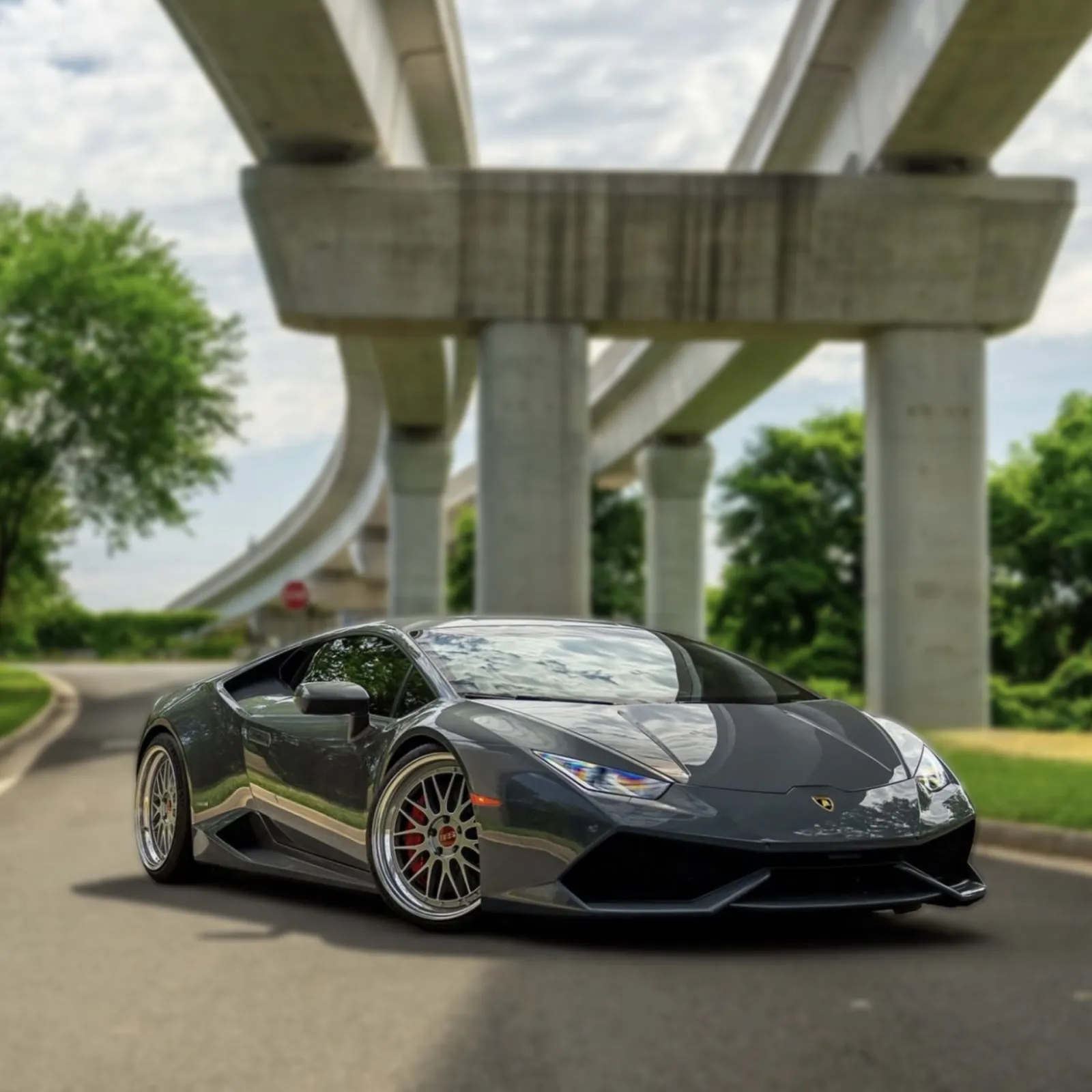 Glossy black Lamborghini sports car parked on road under concrete overpass with trees in background.