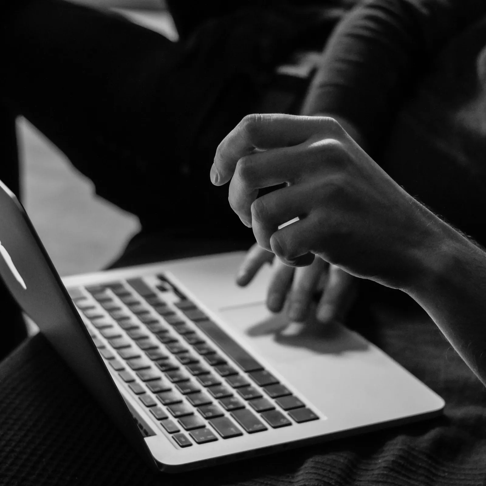 A close-up of a hand typing on a laptop keyboard in black and white, showcasing focus and technology.