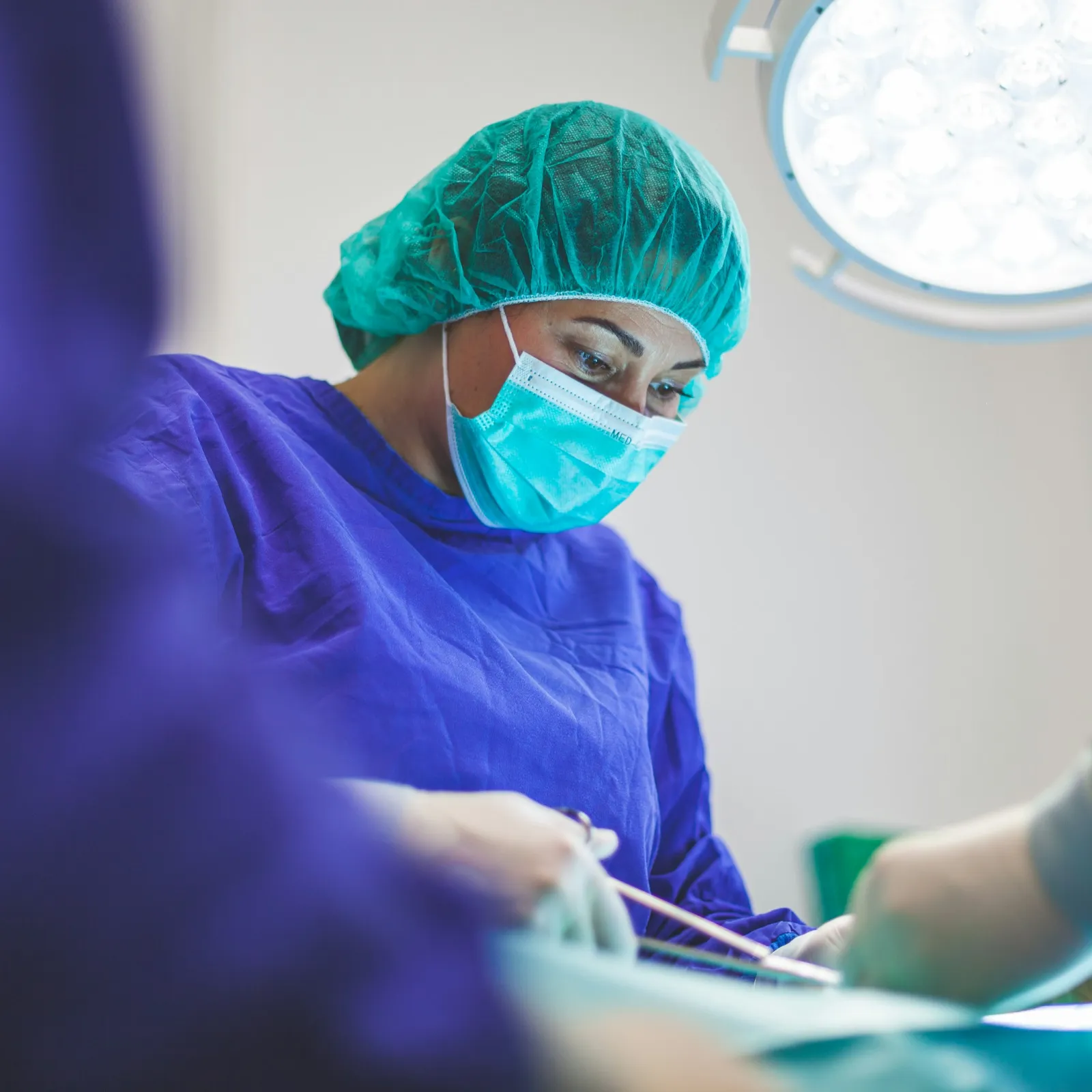 Surgeon in scrubs focusing on surgery under medical lighting.