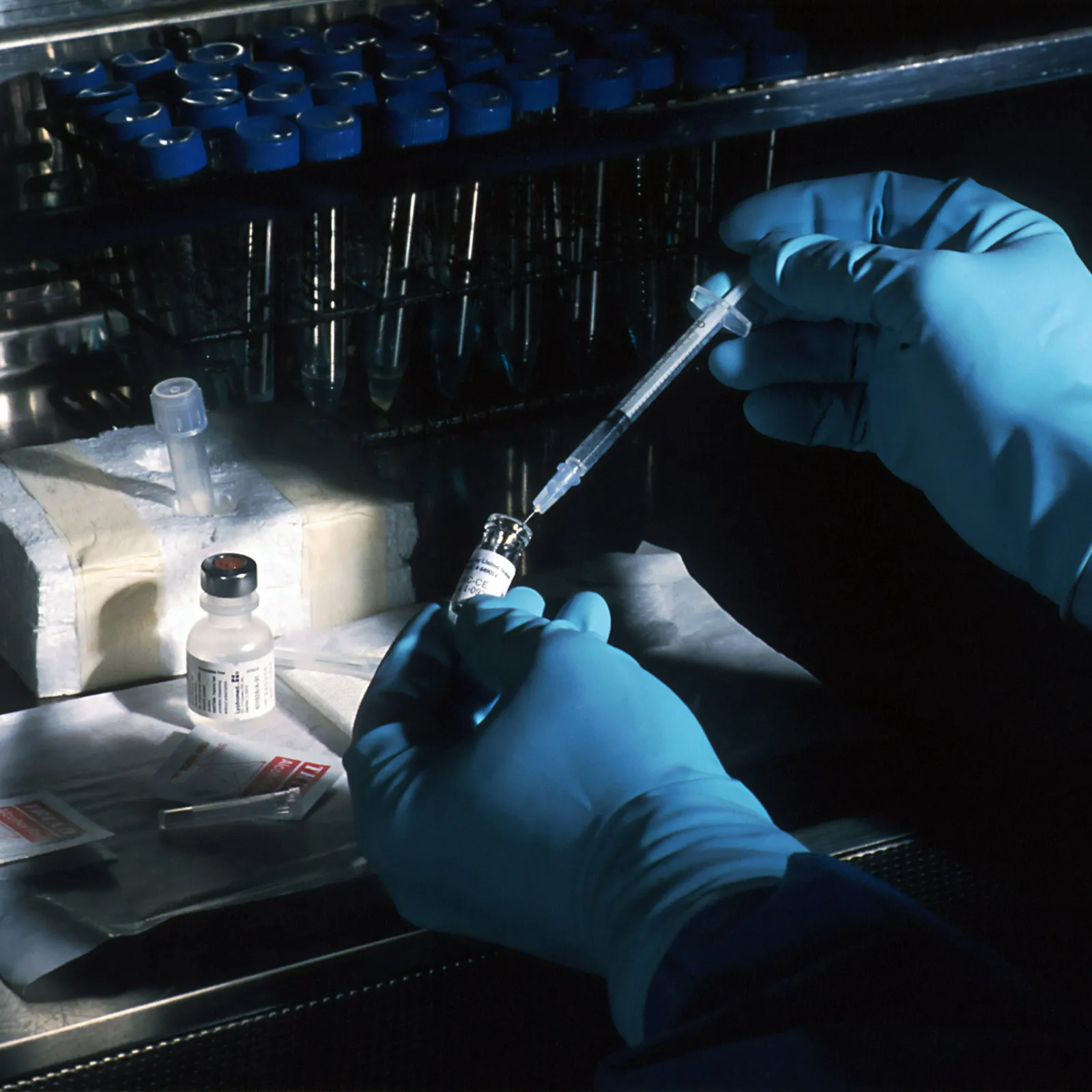 a person in a blue glove and gloves holding a syringe