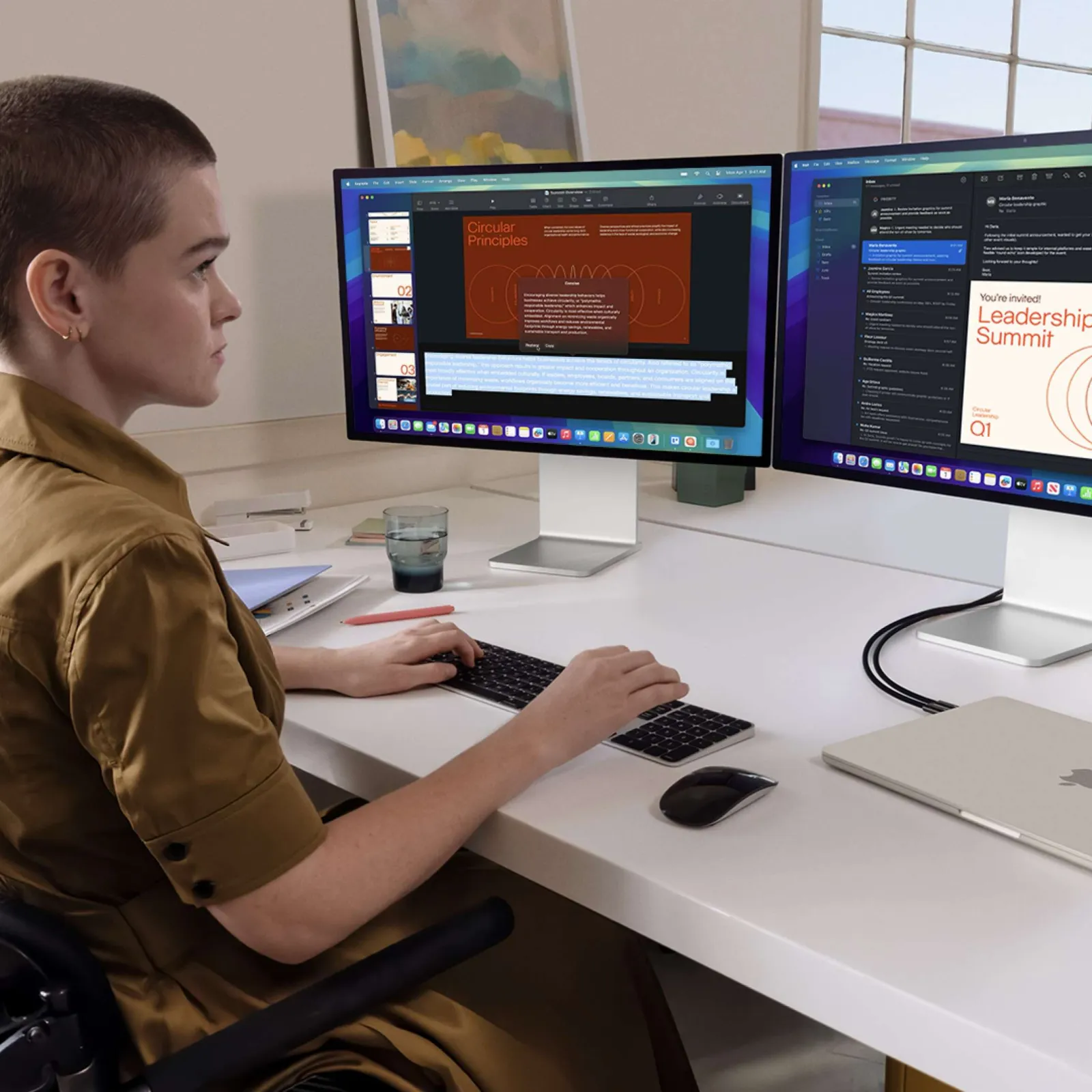 Person with short hair working on dual monitors at a clean white desk with a laptop and keyboard.