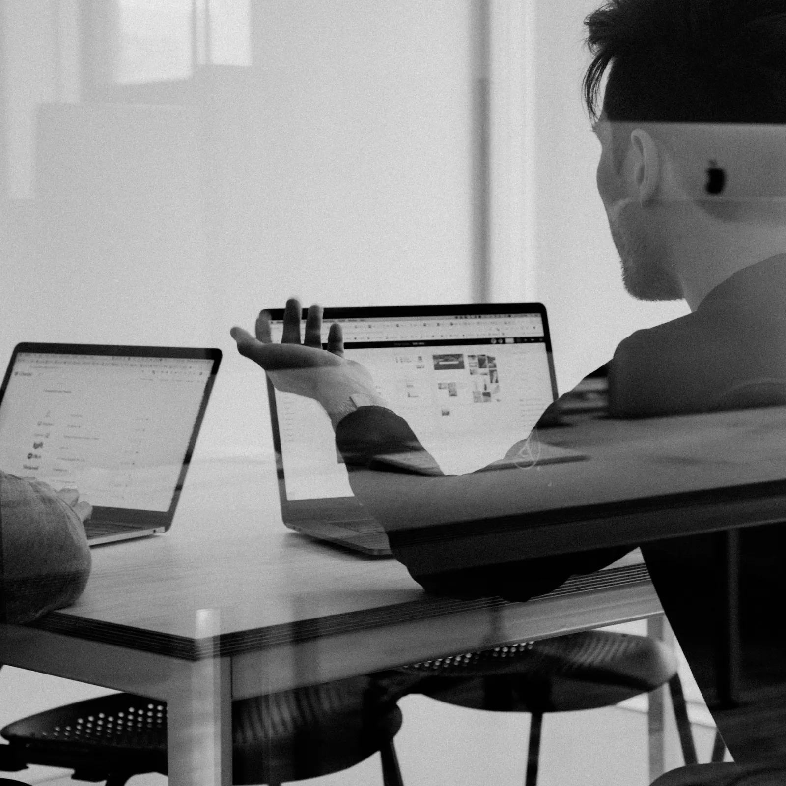 Two people in a meeting discussing ideas on laptops in a modern office setting.