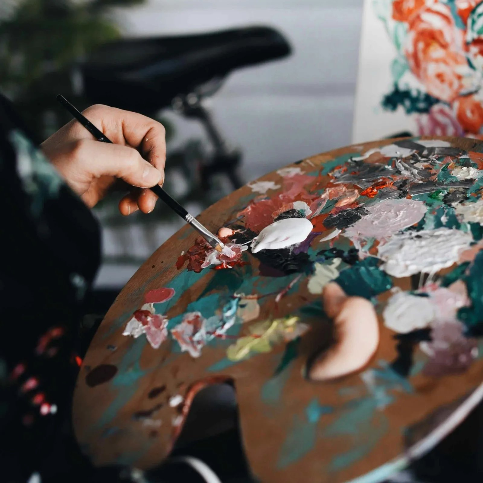 A hand holding a brush over a colorful artist's palette with vibrant paint blobs.