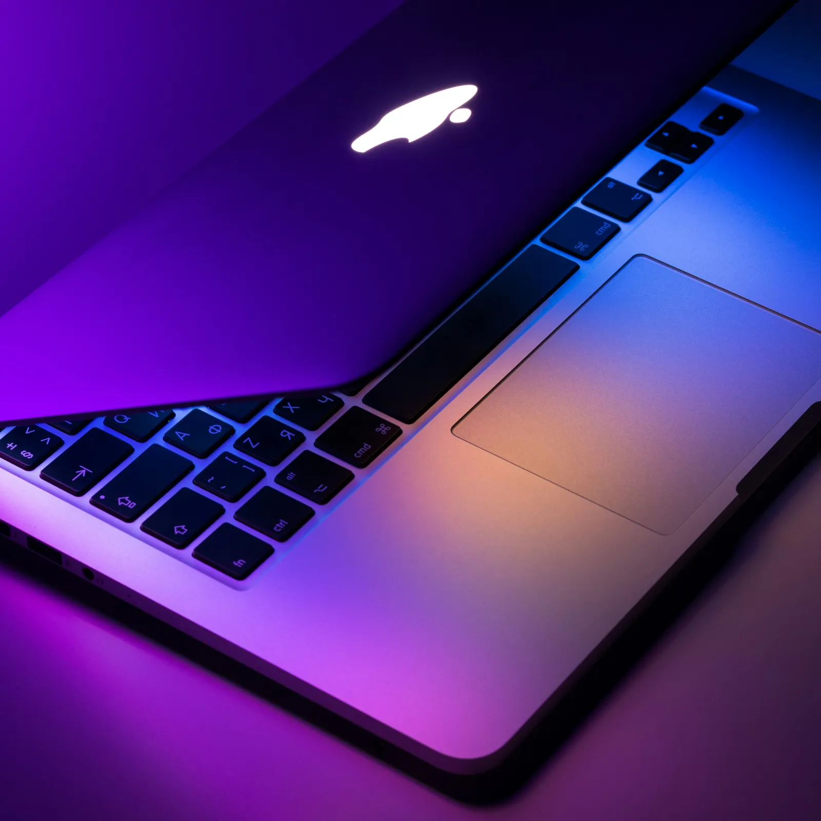 Close-up of a MacBook keyboard illuminated by colorful lighting.