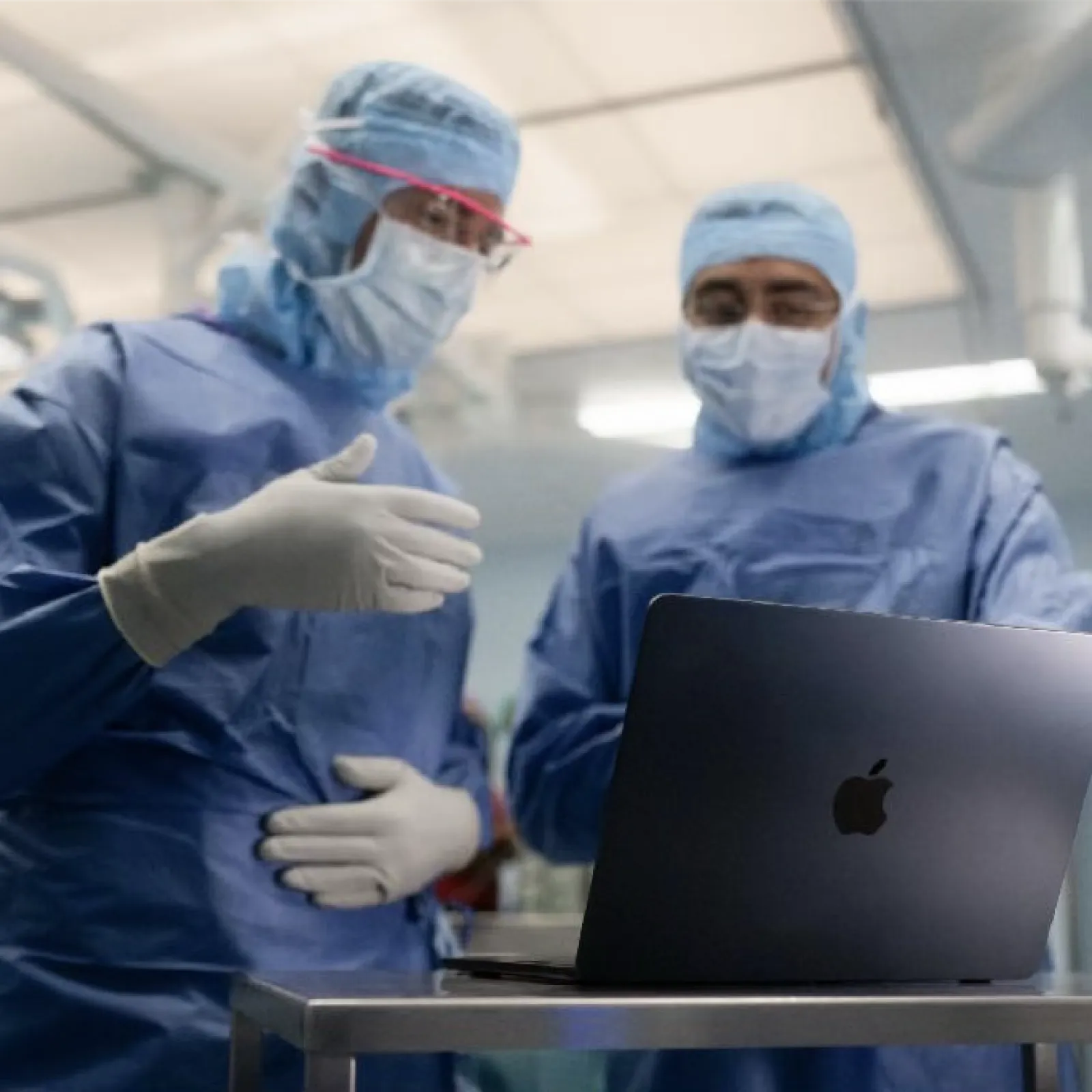Two surgeons in blue scrubs and gloves reviewing information on a laptop in an operating room.