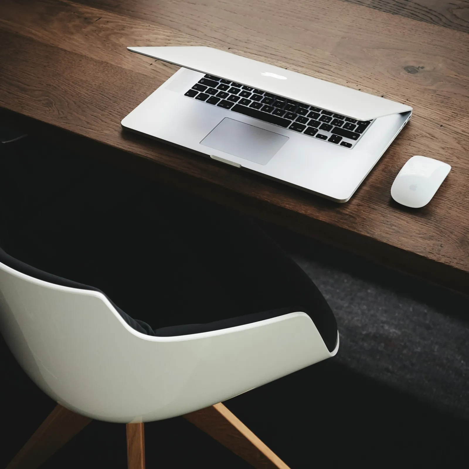 Minimalist workspace featuring a MacBook and a sleek chair on a wooden desk.