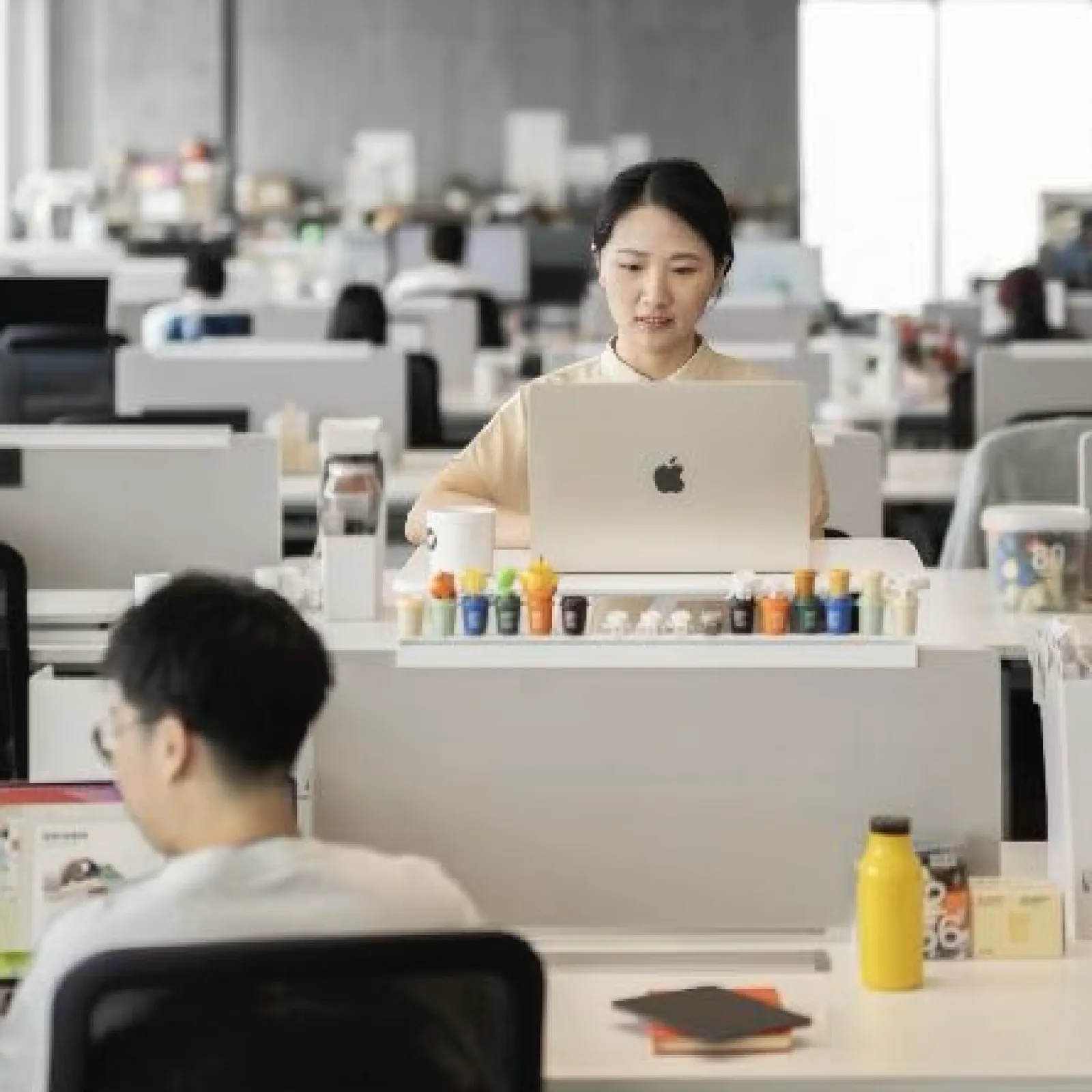 Open office with diverse employees working on laptops and computers in a modern workspace.