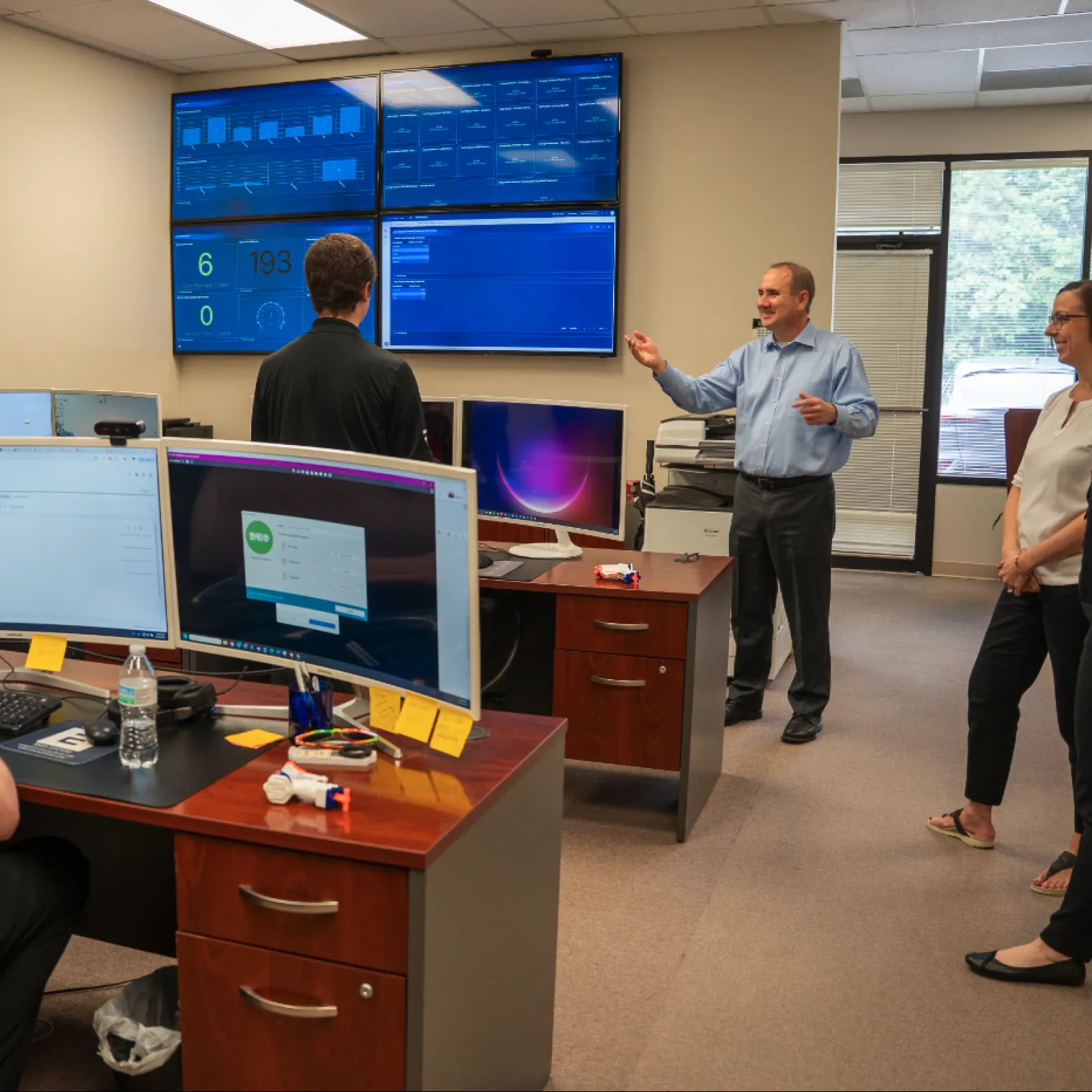 IT team discussing data and monitoring on multiple screens in a modern office workspace with large display monitors.