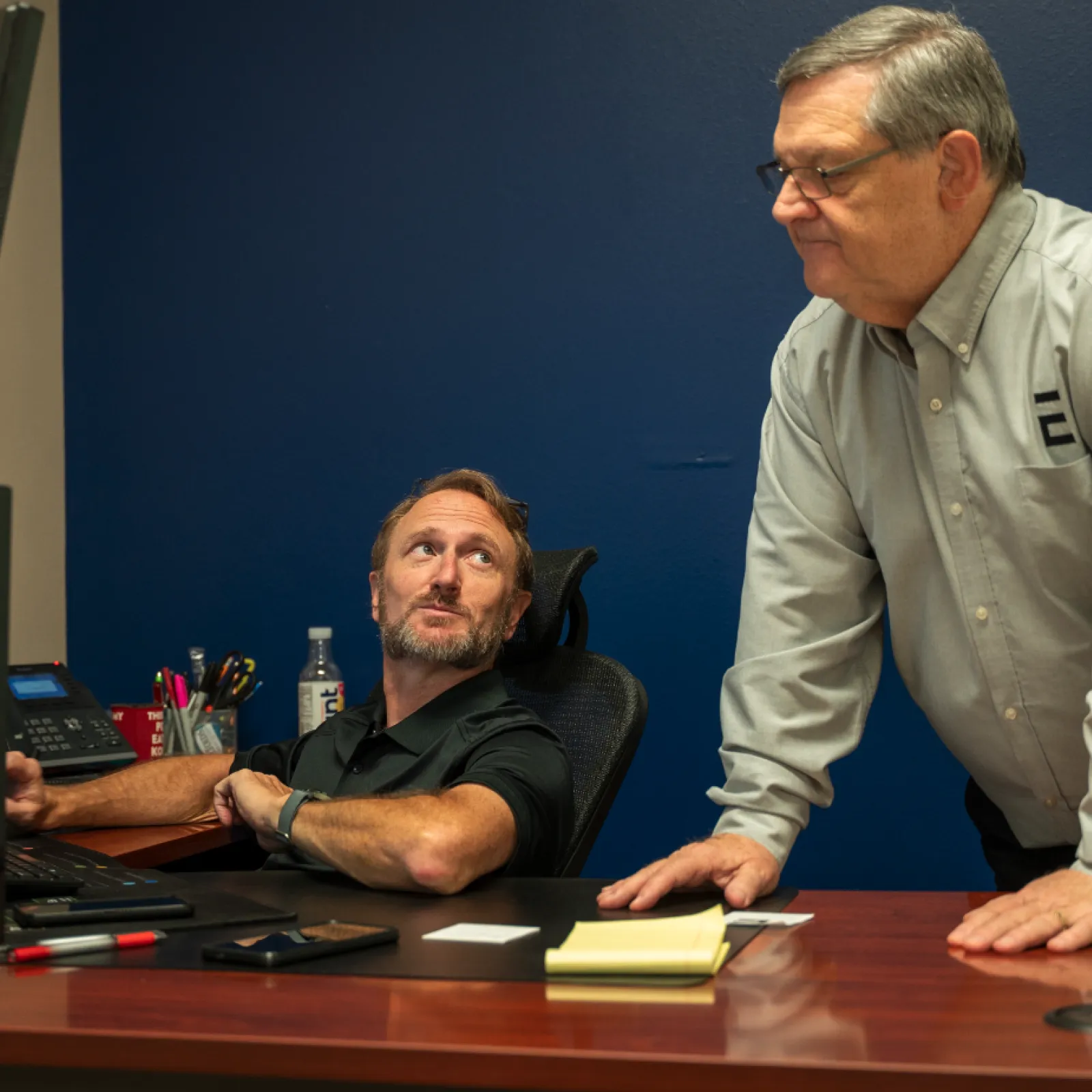 Two men collaborating at a desk with multiple monitors in a modern office setting