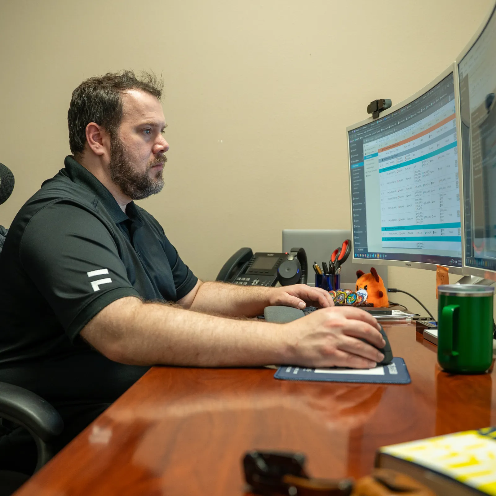 Man focused on computer screens working at a wooden desk in a modern office setting