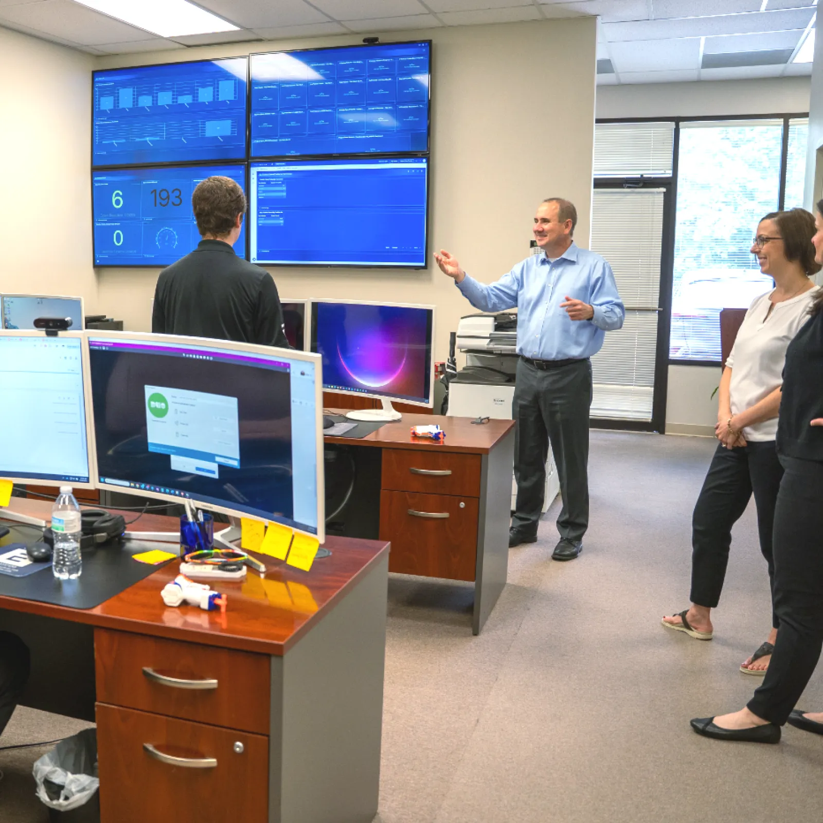 Team meeting in office with multiple computer monitors and data dashboards on wall screens