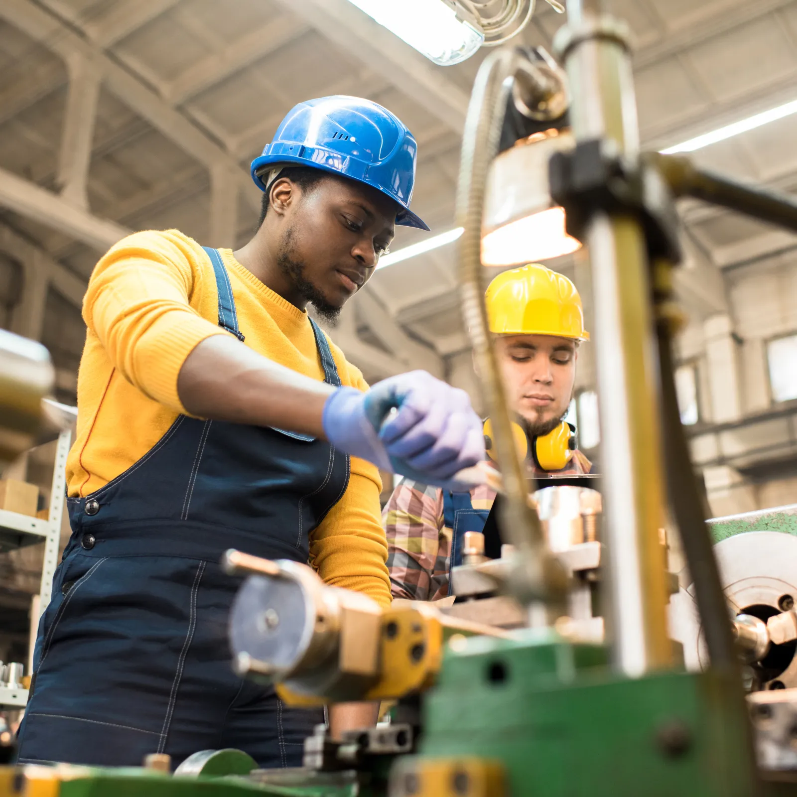 Three men having a conversation inside an industrial workshop with machinery and tools.
