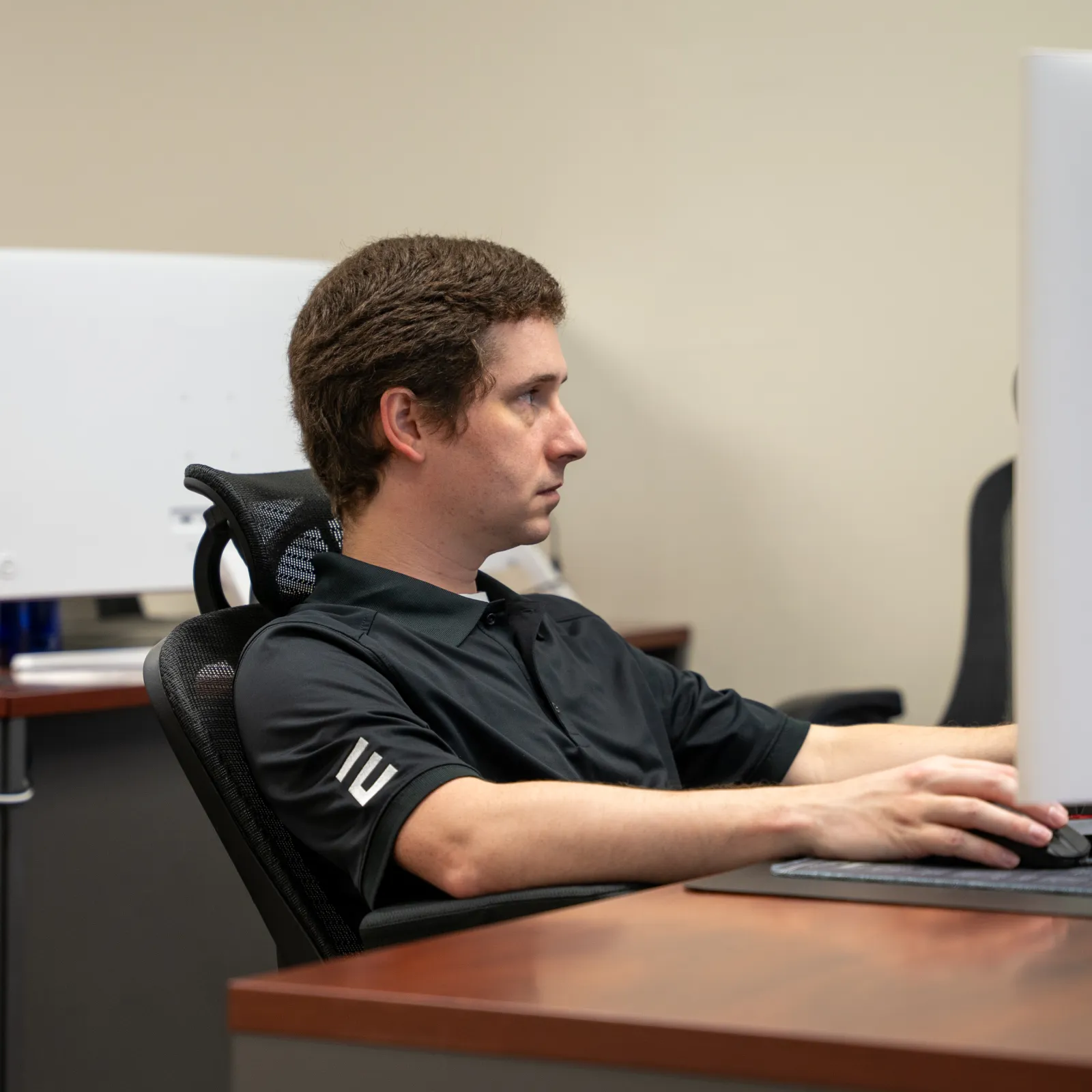 Man focused at computer workstation in office setting with multiple monitors and sparse decor