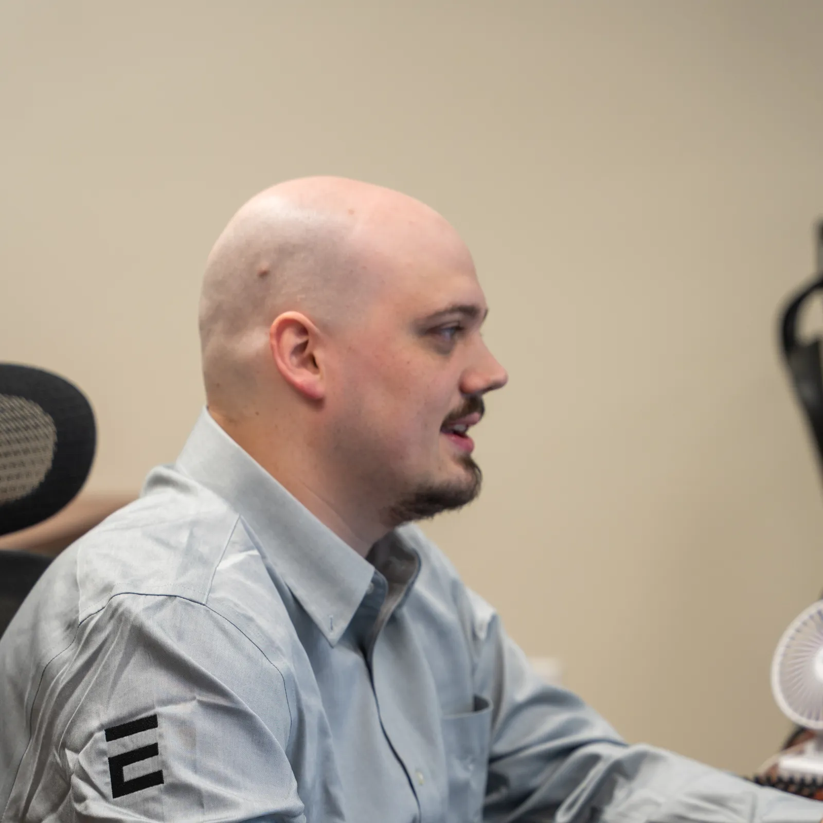 Bald man in a gray shirt working at a desk with a notebook and water bottle in an office setting.