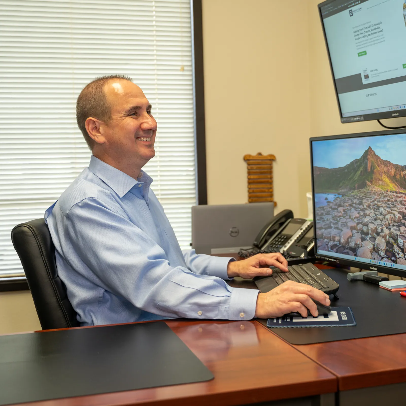 Man in blue shirt working on a desktop computer with multiple monitors in an office setting