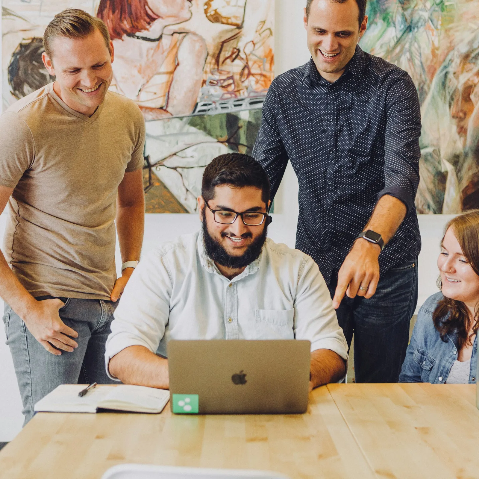 a group of people standing around a table with laptops