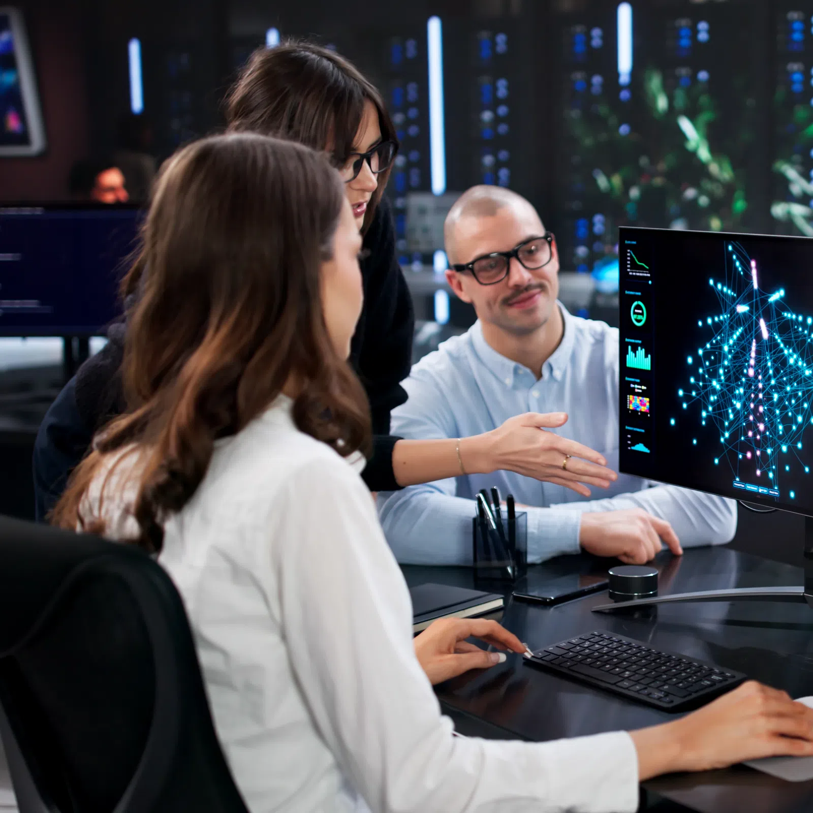 Team of software developers analyzing data visualization and code on dual monitors in modern office environment.