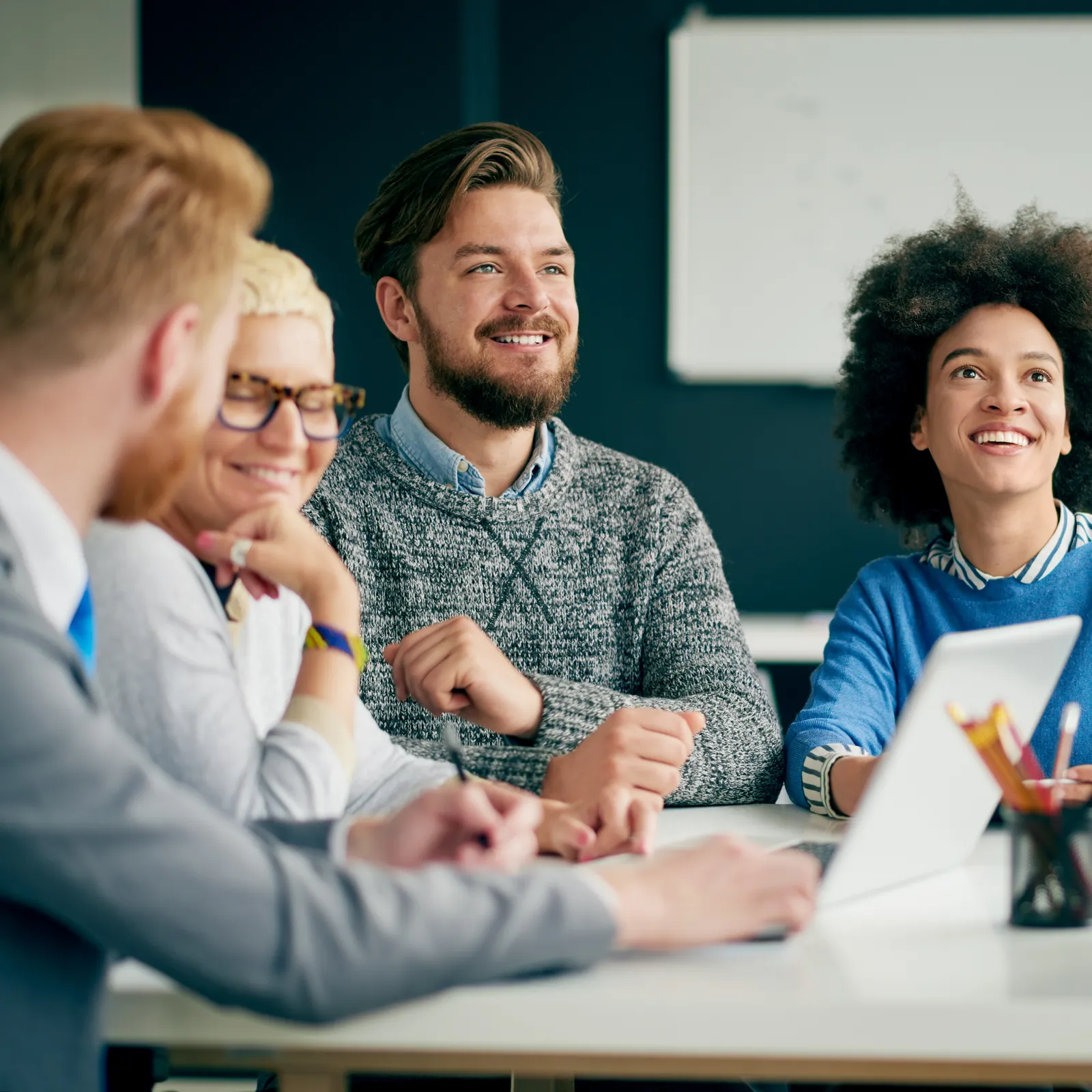 A diverse group of young professionals engaged in a collaborative meeting, smiling and discussing ideas.