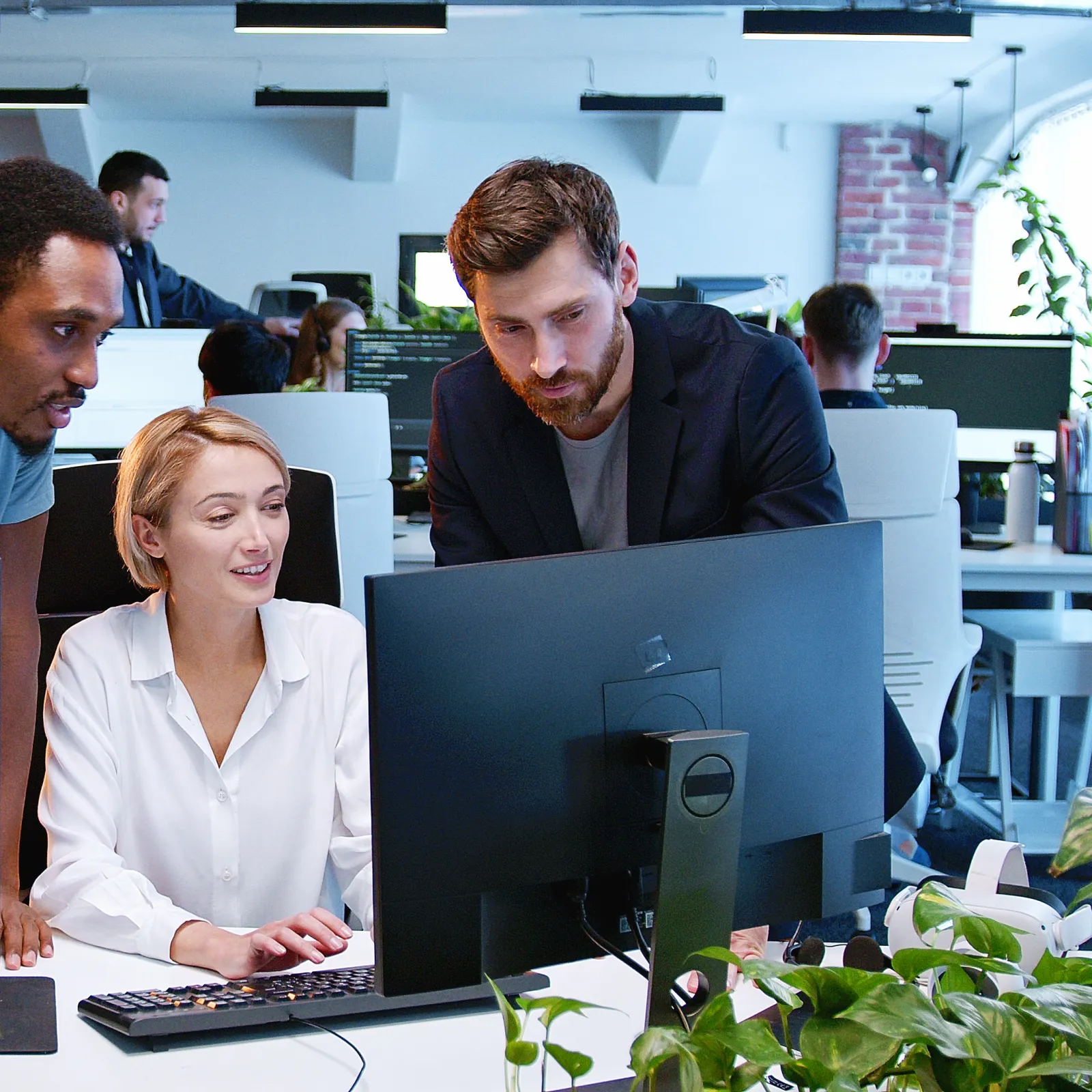 Three colleagues collaborating in a modern office space filled with plants and computers.