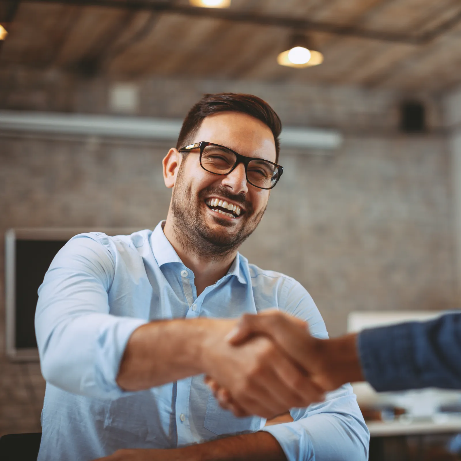Two professionals shaking hands in an office setting, smiling and engaging in a friendly discussion.