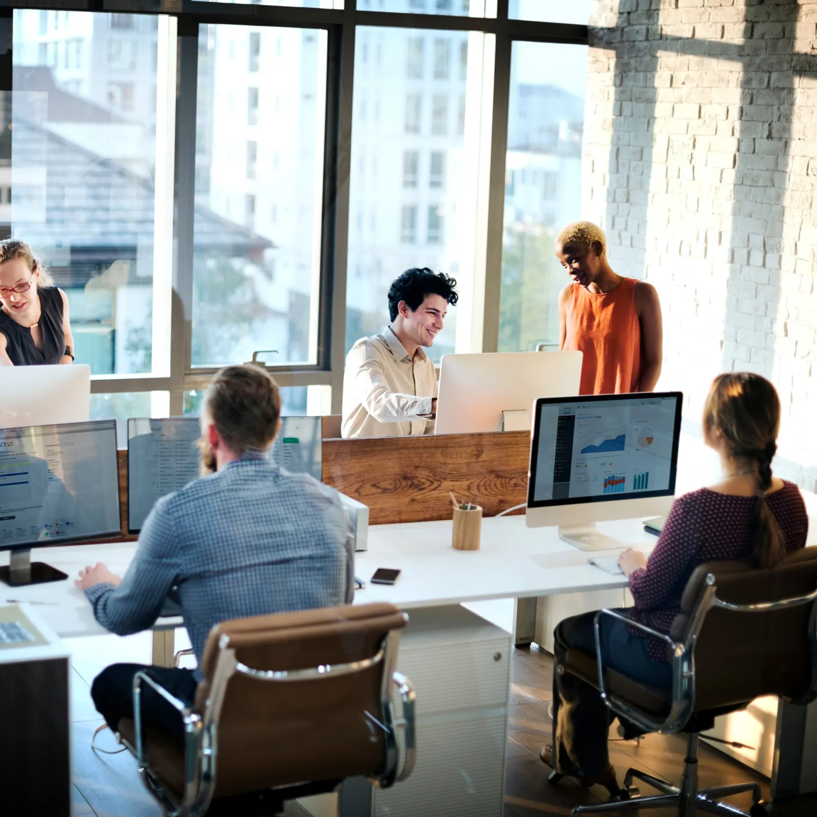 A diverse team collaborates in a modern office space with computers and natural light.