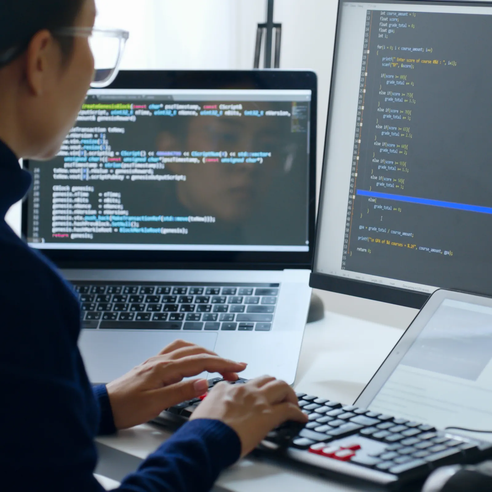Person coding on laptop and desktop with code displayed on screens in a modern workspace.