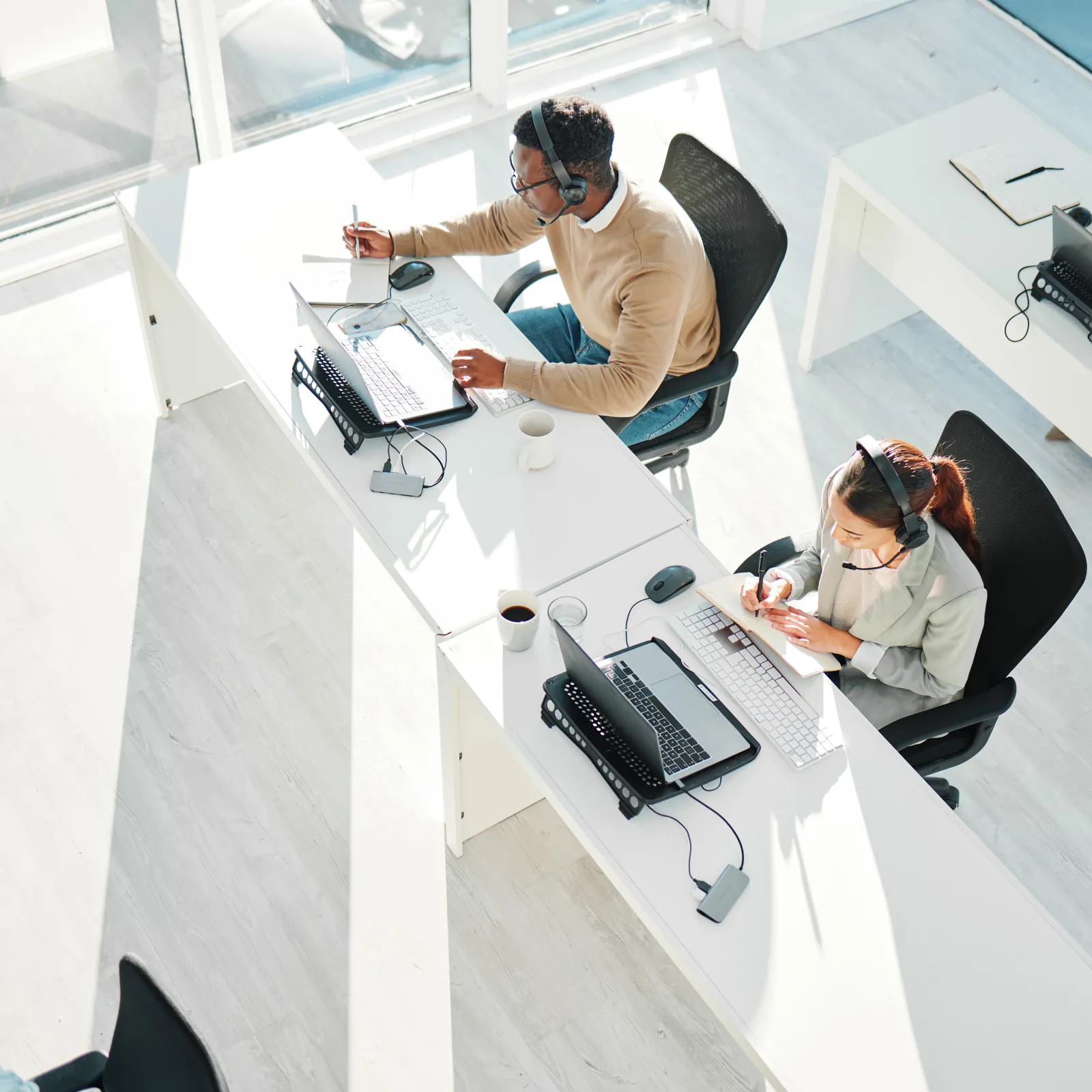 A modern office with employees working at desks using computers and headsets in a bright environment.