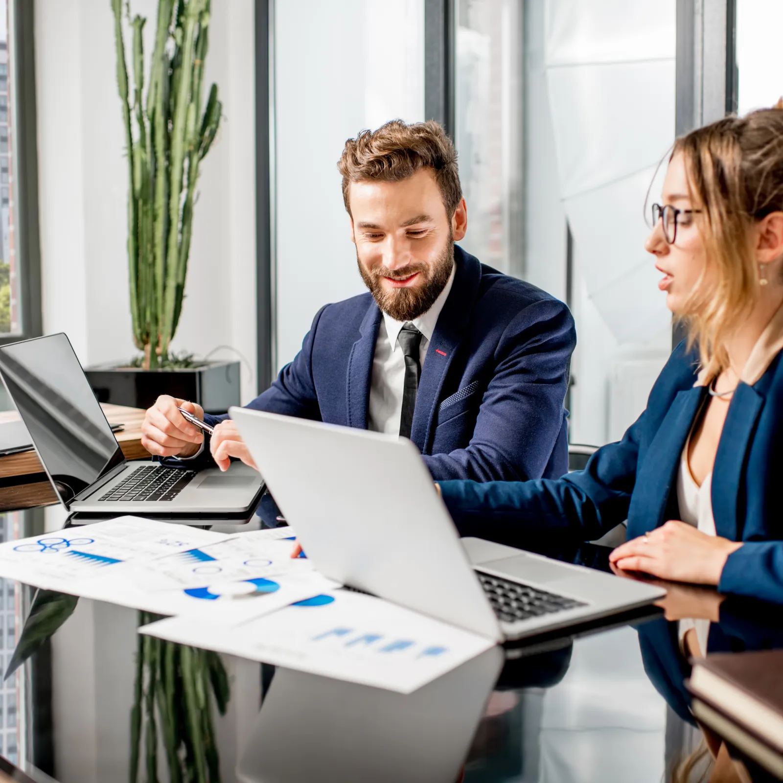Two professionals discussing charts and data in a modern office environment with laptops.
