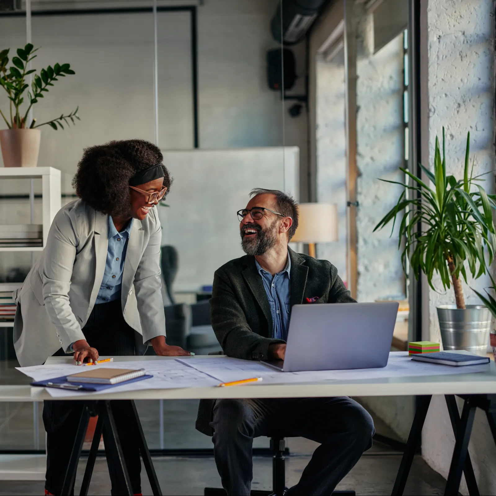 Two professionals collaborating in a modern office with plants and bright decor.