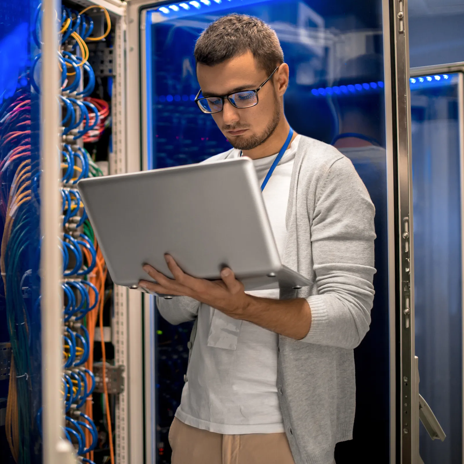 IT professional working on a laptop in a server room with colorful cables.